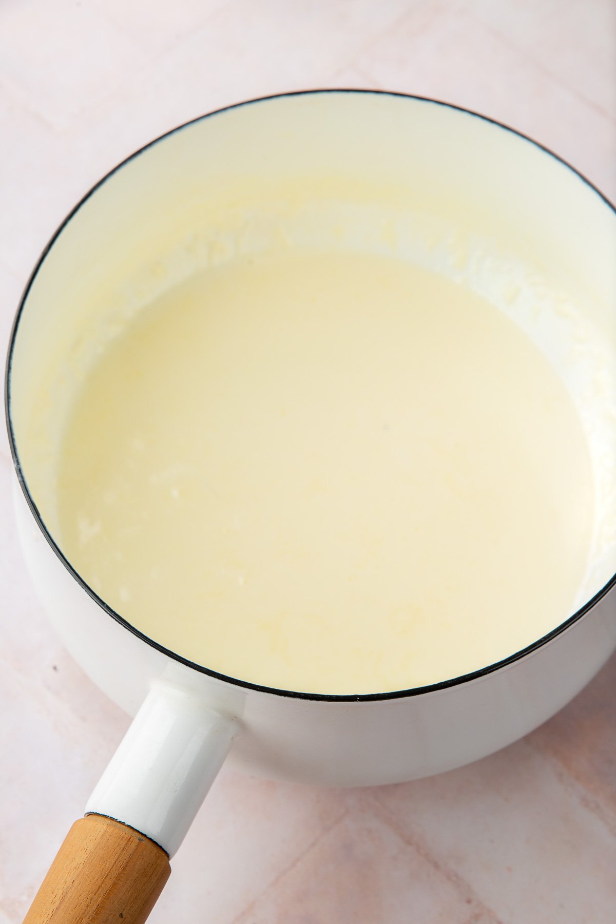 A white saucepan with heavy cream simmering in it.