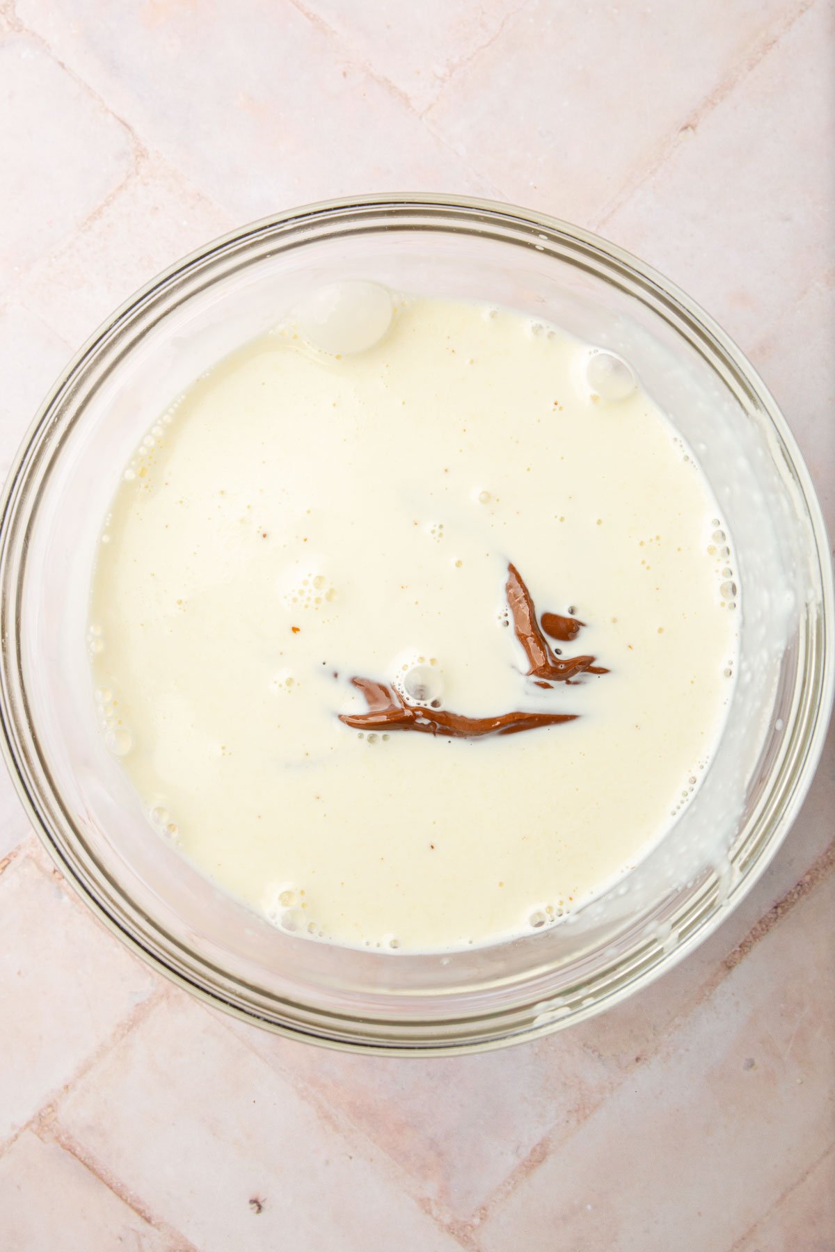 A glass mixing bowl with Nutella covered in warm heavy cream before mixing together.