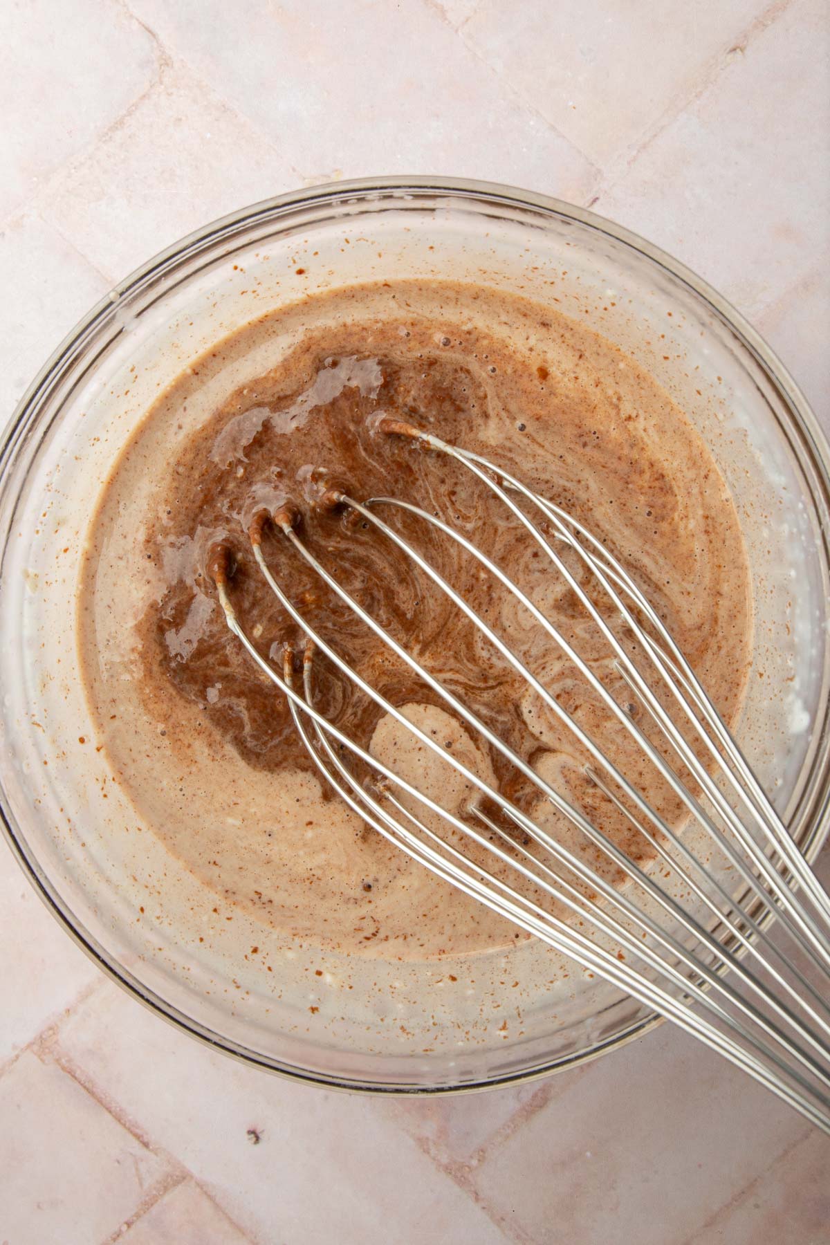 a glass mixing bowl of warm heavy cream and Nutella being whisked together.