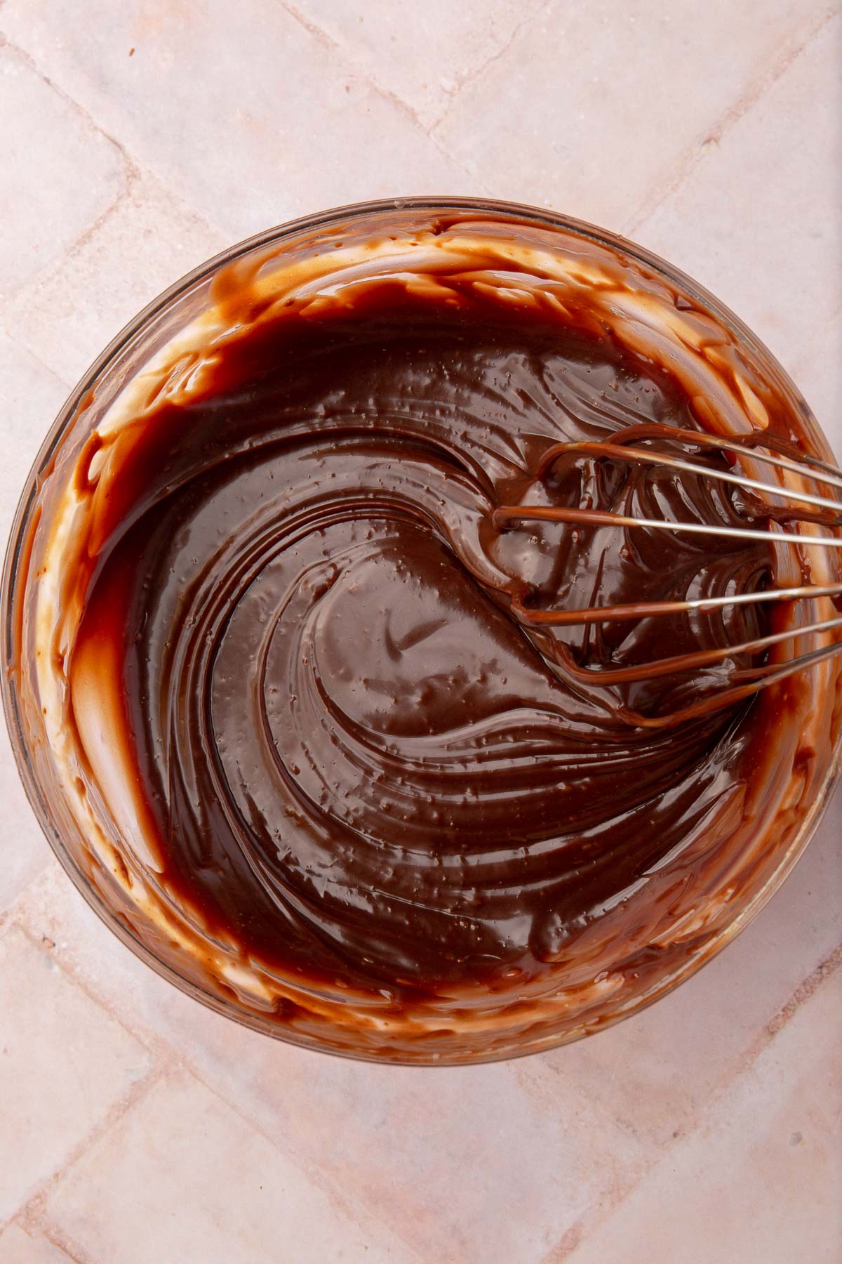 A close up shot of Nutella ganache being whisked with a wire whisk in a glass mixing bowl.
