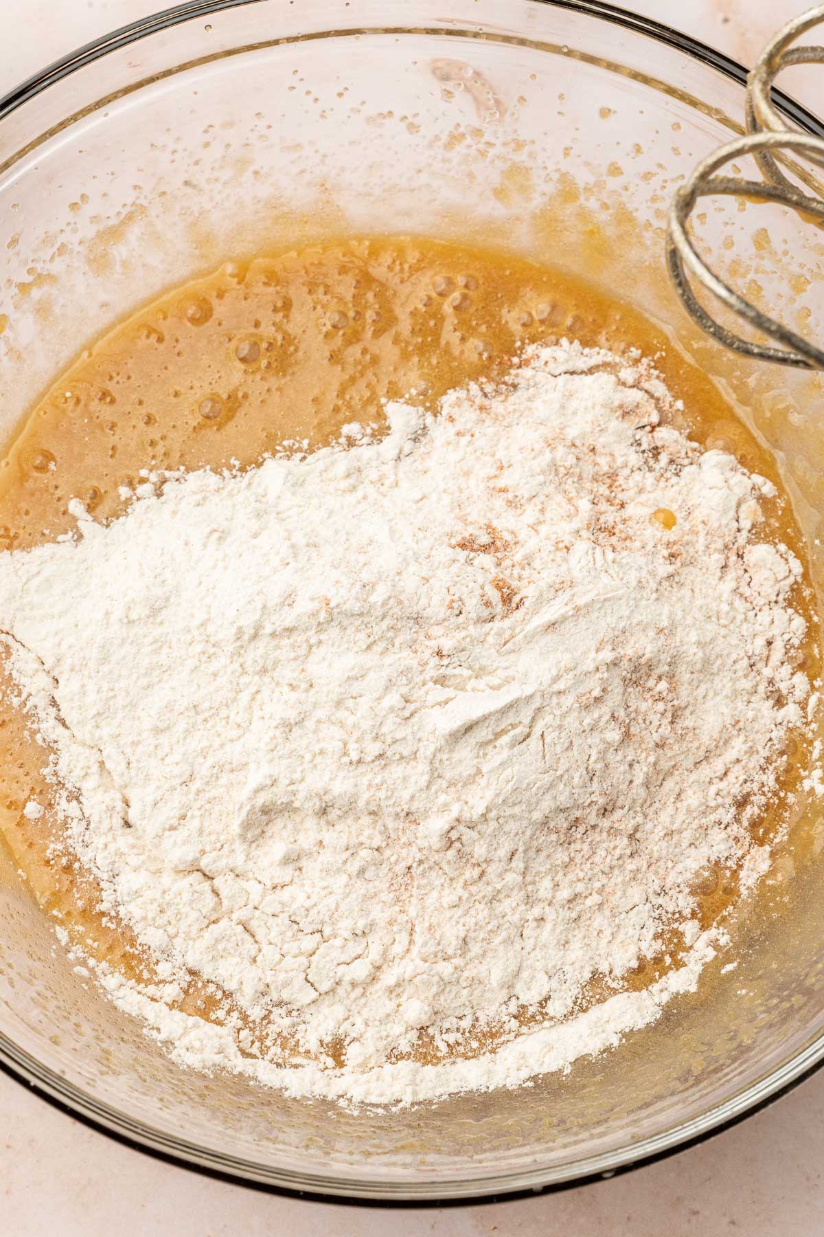 A glass mixing bowl with gluten-free cookie dough topped with gluten-free flour before mixing together.