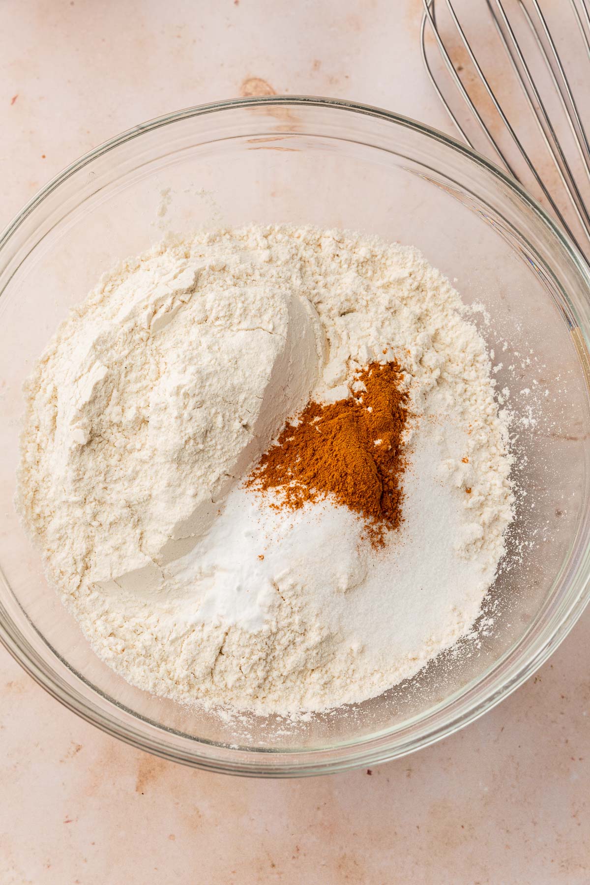 A glass mixing bowl with gluten-free flour, cinnamon, salt and baking soda in it before mixing together.