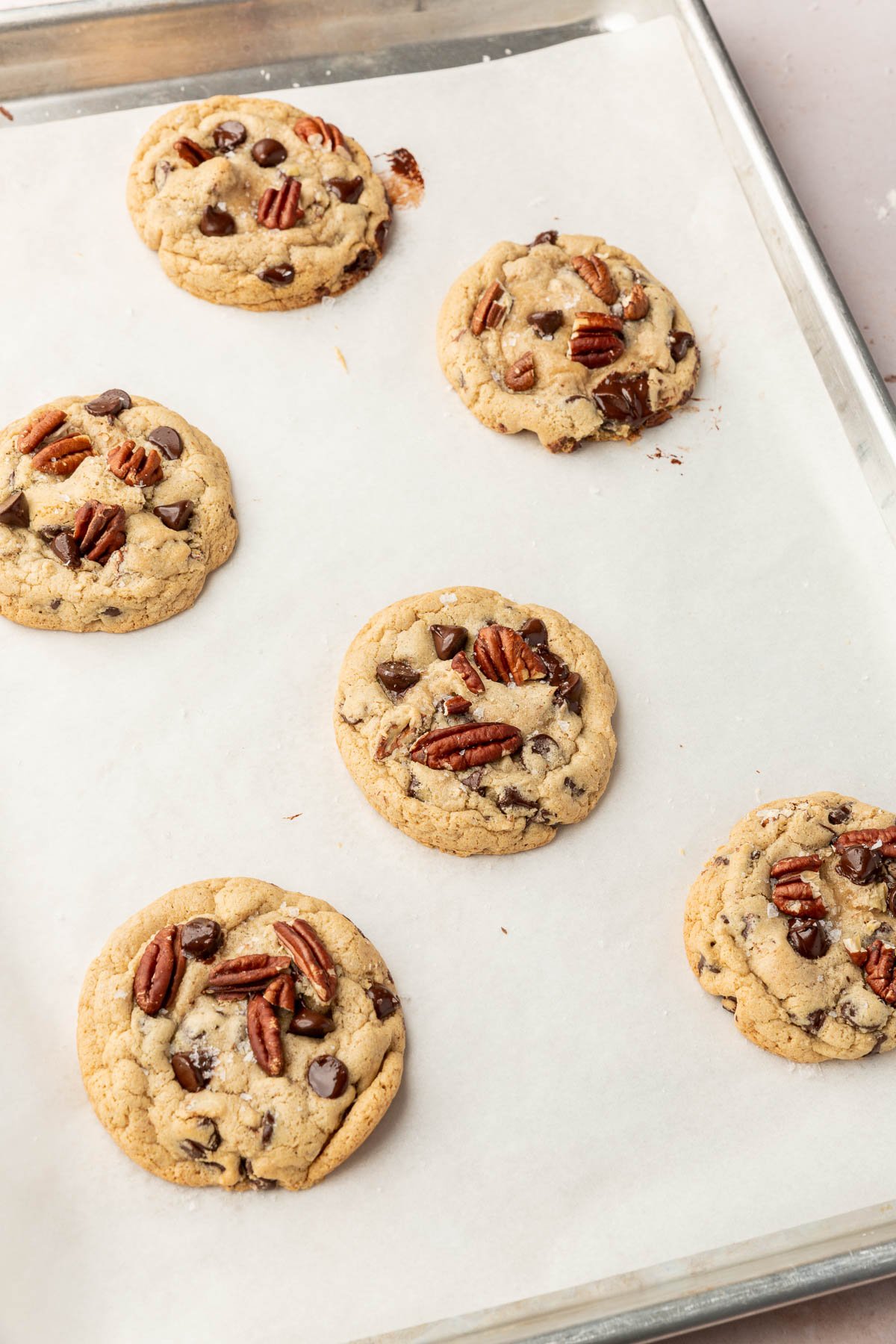 Six gluten-free pecan chocolate chip cookies on a baking sheet lined with parchment paper.