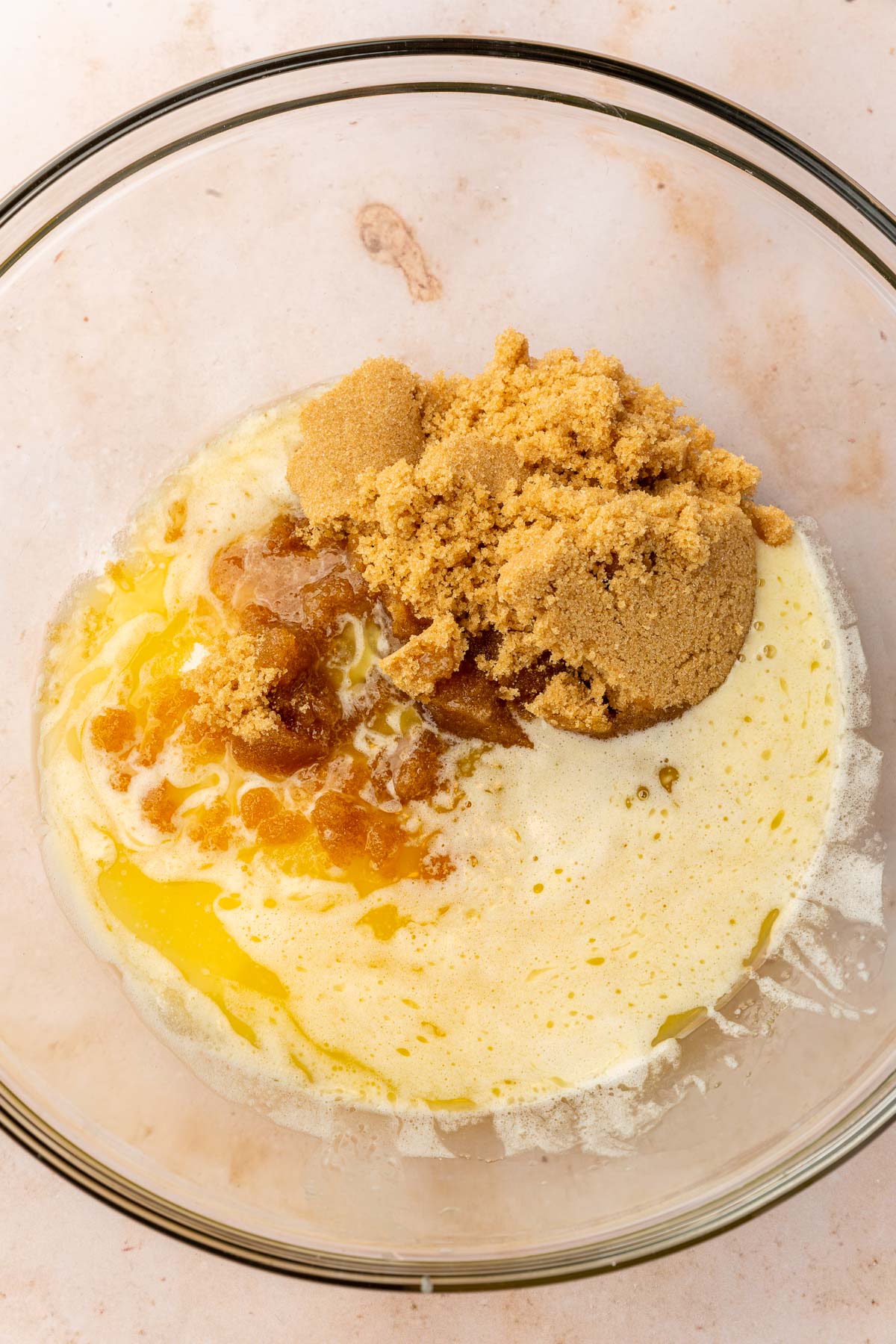 A glass mixing bowl with melted butter topped with brown sugar and granulated sugar.