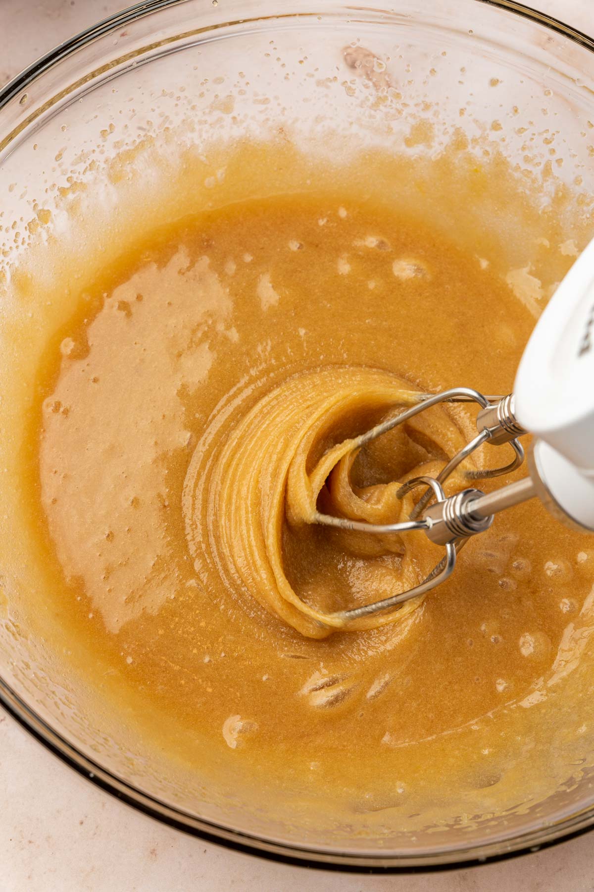 An electric mixer mixing together a cookie dough mixture of melted butter, brown sugar, sugar, vanilla, and eggs.
