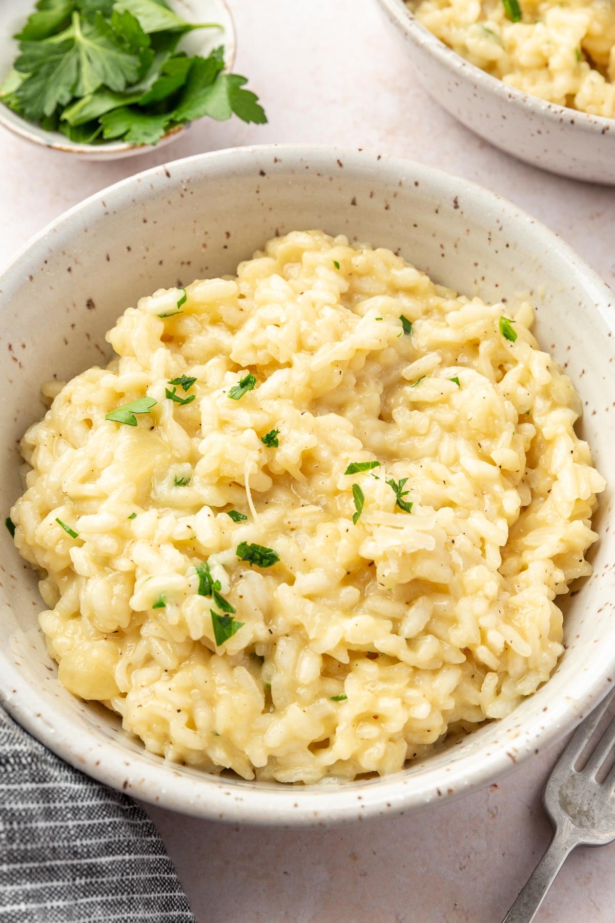 A bowl of gluten free risotto topped with finely chopped parley with additional parsley in the background.