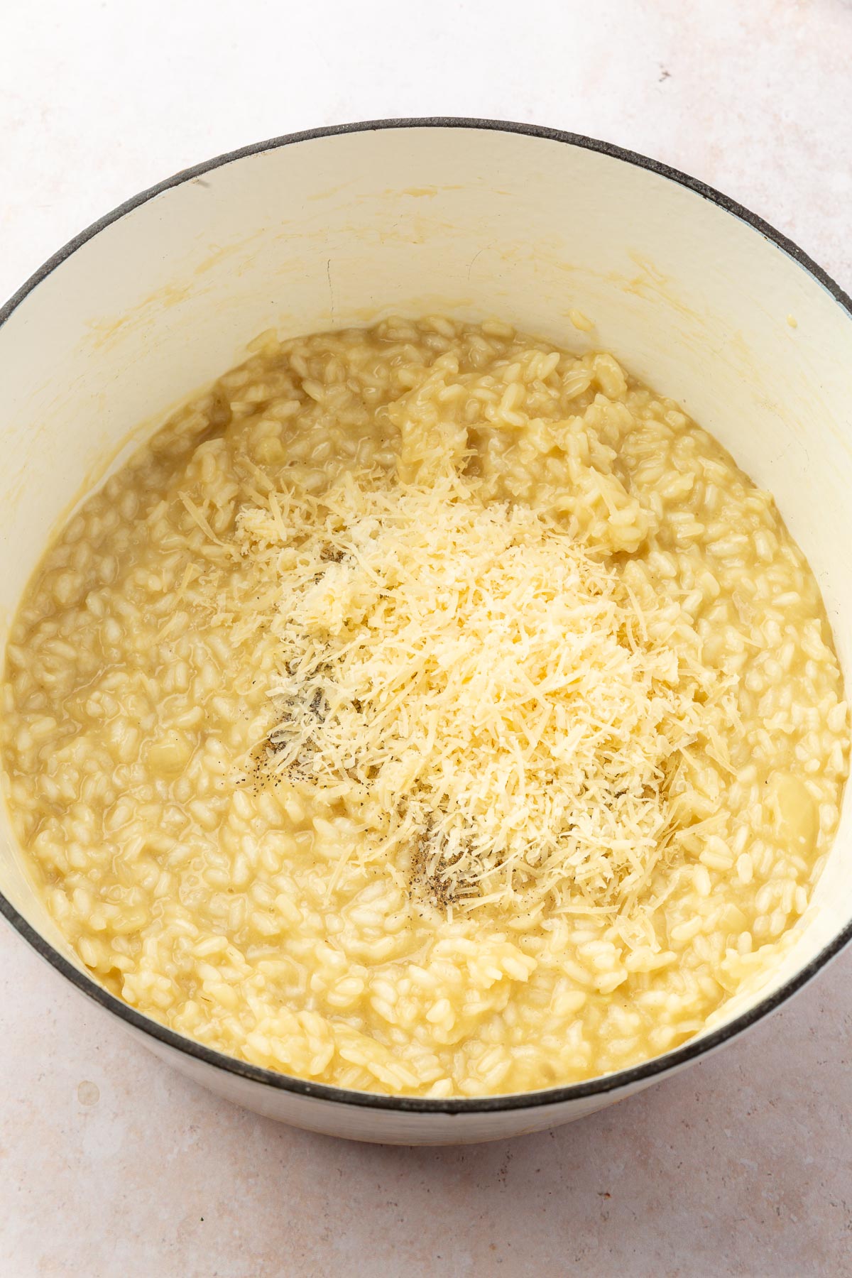 A white dutch oven filled with creamy risotto topped with ground black pepper and shredded parmesan cheese.