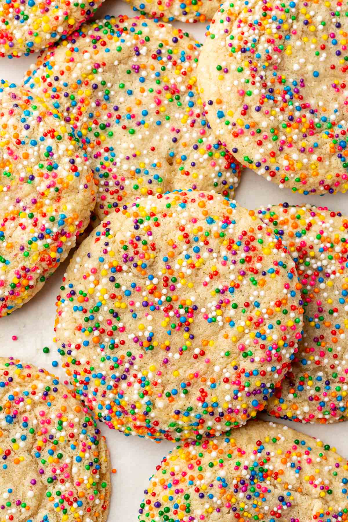 Gluten-free sprinkles sugar cookies overlapping each other on a piece of parchment paper.