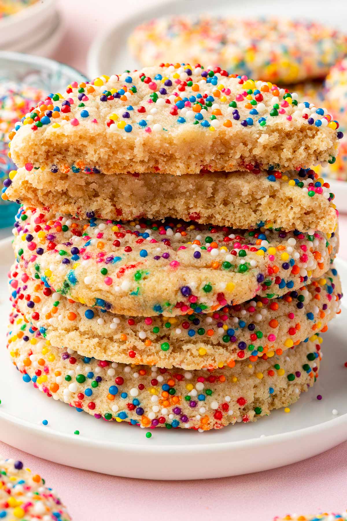 A stack of gluten-free sprinkles sugar cookies with the top two sliced in half to see the chewy insides.