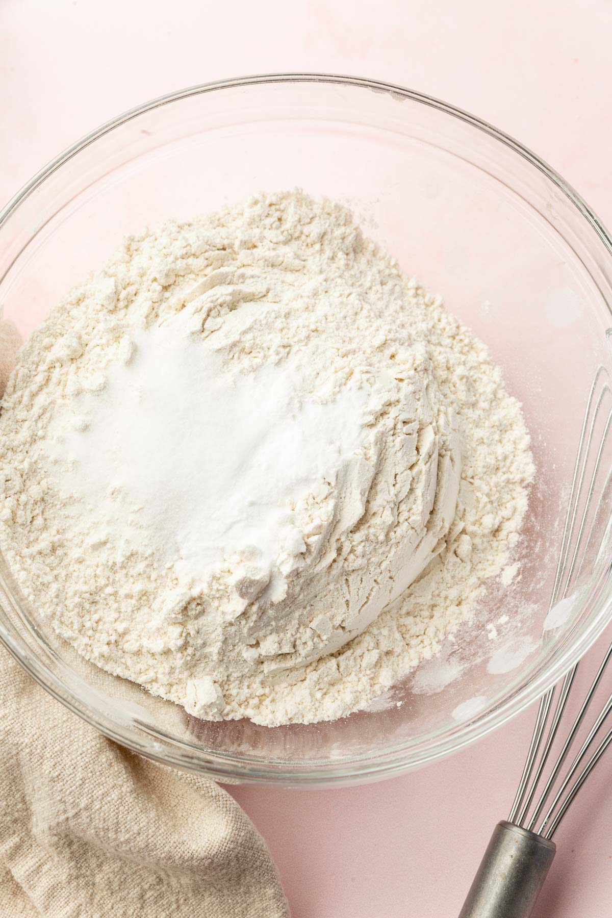 A glass mixing bowl with a gluten-free flour blend topped with salt and baking soda before whisking together.