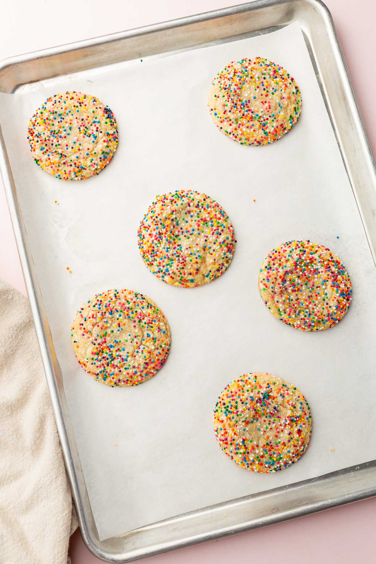 A baking sheet lined with parchment paper and topped with six gluten free sprinkle sugar cookies that have been baked in the oven.