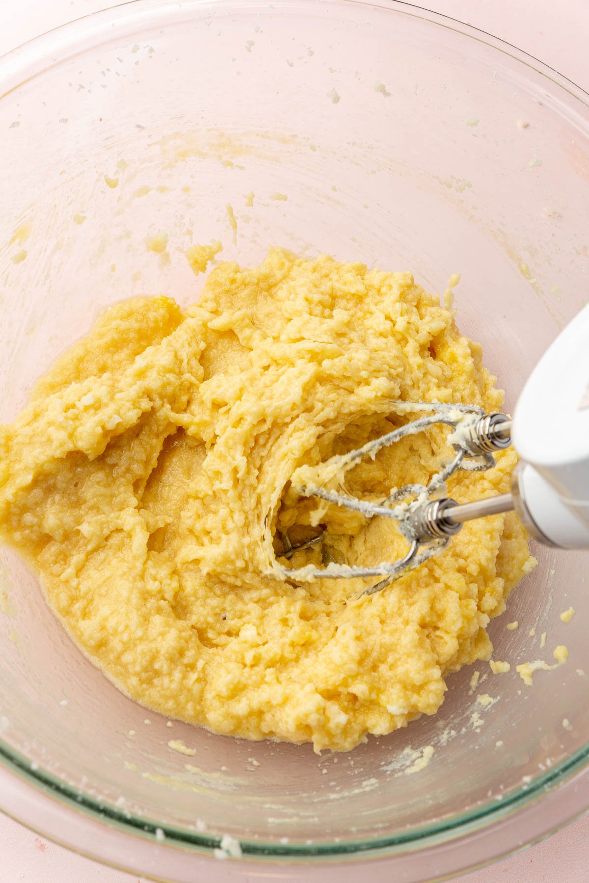 An electric mixer mixing a butter, sugar and egg mixture in a glass bowl to make cookie dough.