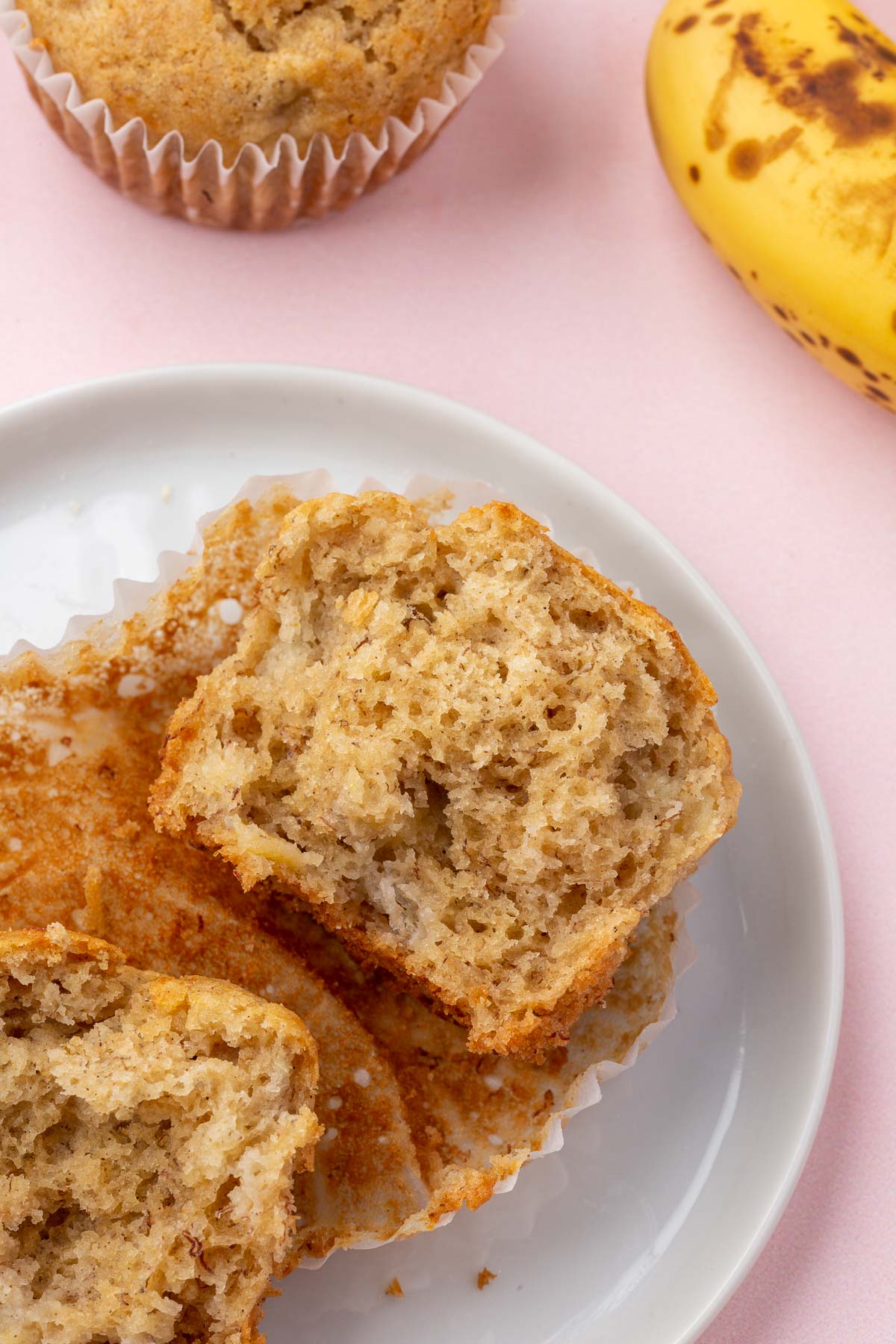 A gluten-free banana muffin on a small dessert plate that has been torn in half to see the inside texture of the muffin.