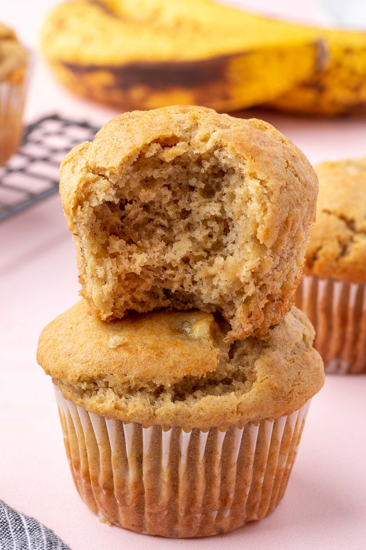 Two gluten-free banana muffins stacked on top of each other with the top one having a bite taken out of it.