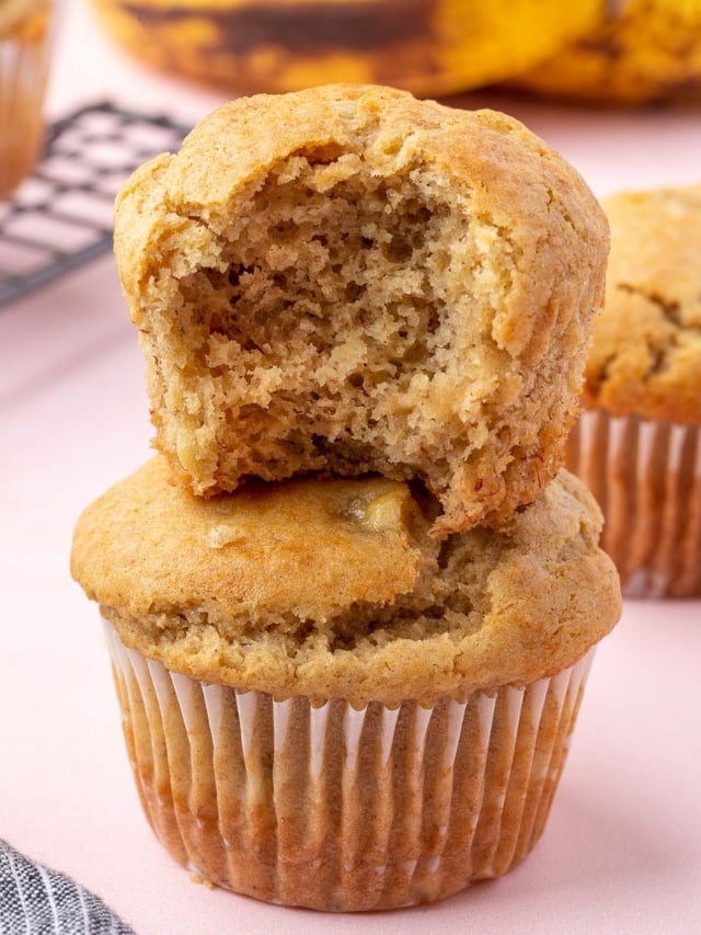 A stack of two gluten-free banana muffins with the top one having a bite taken out of it.