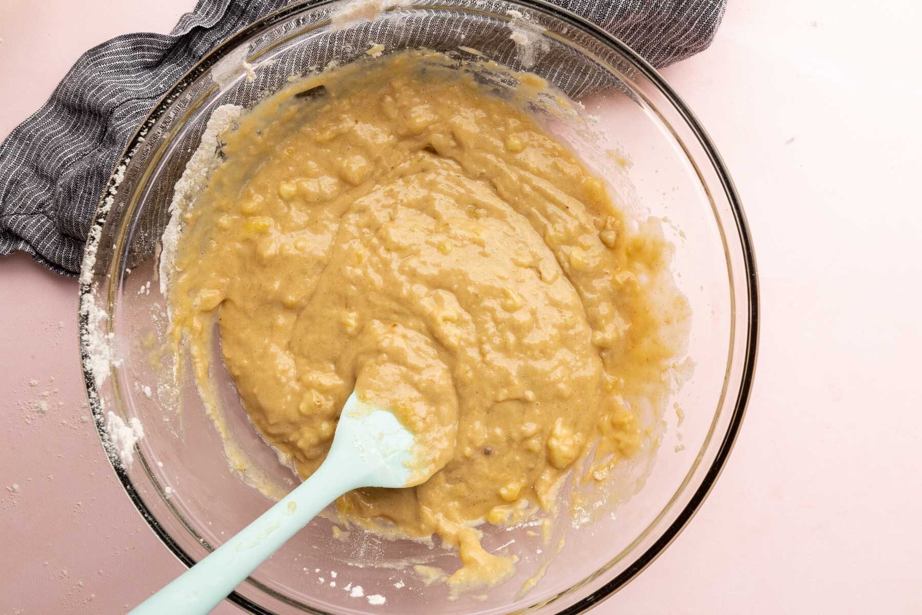 A glass mixing bowl with gluten-free banana batter with a blue spatula.