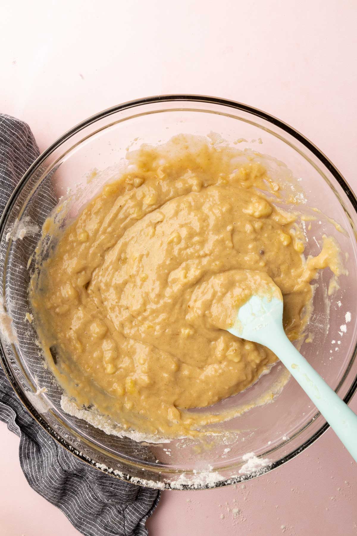 A glass mixing bowl with gluten-free banana batter with a blue spatula.