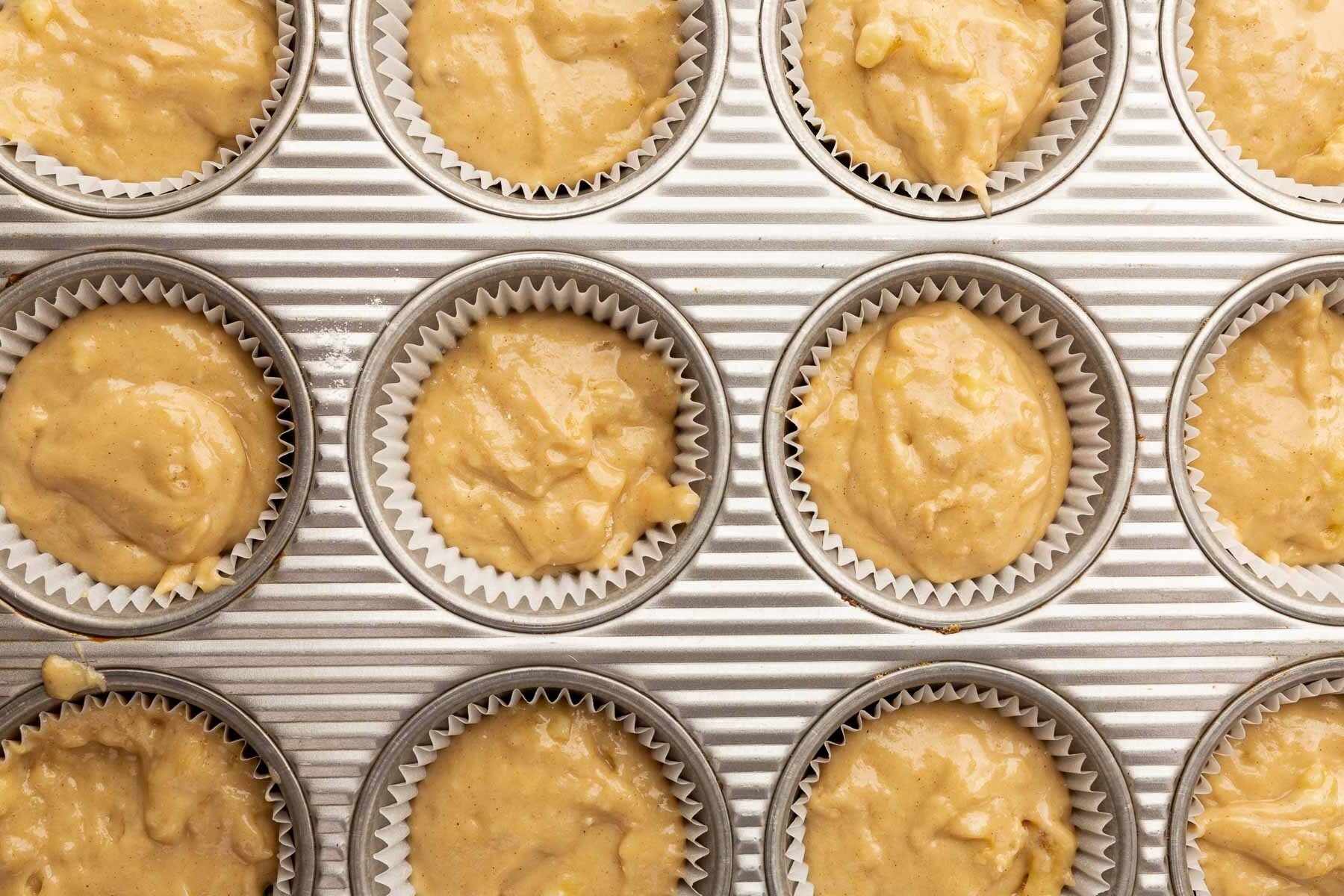 A close of up twelve muffin cups filled with gluten-free banana muffin batter before baking in the oven.