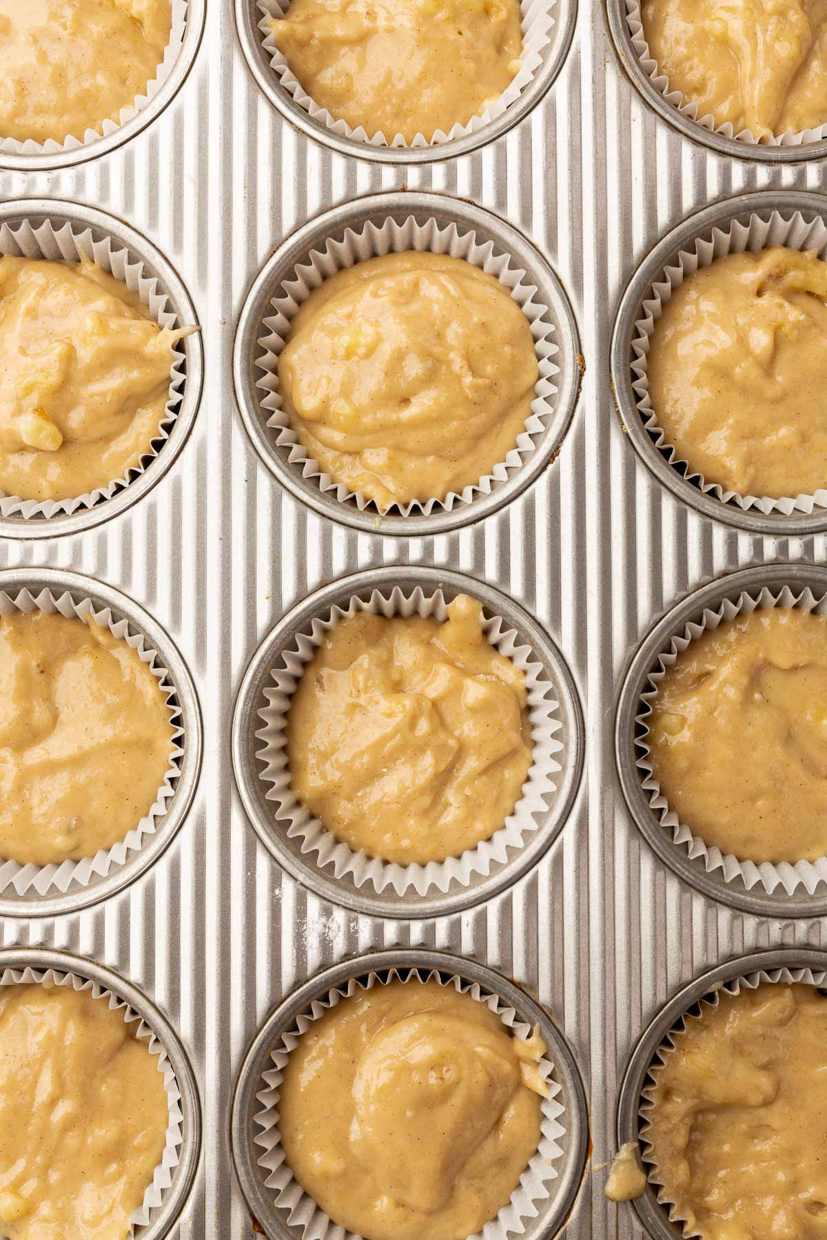 A close of up twelve muffin cups filled with gluten-free banana muffin batter before baking in the oven.