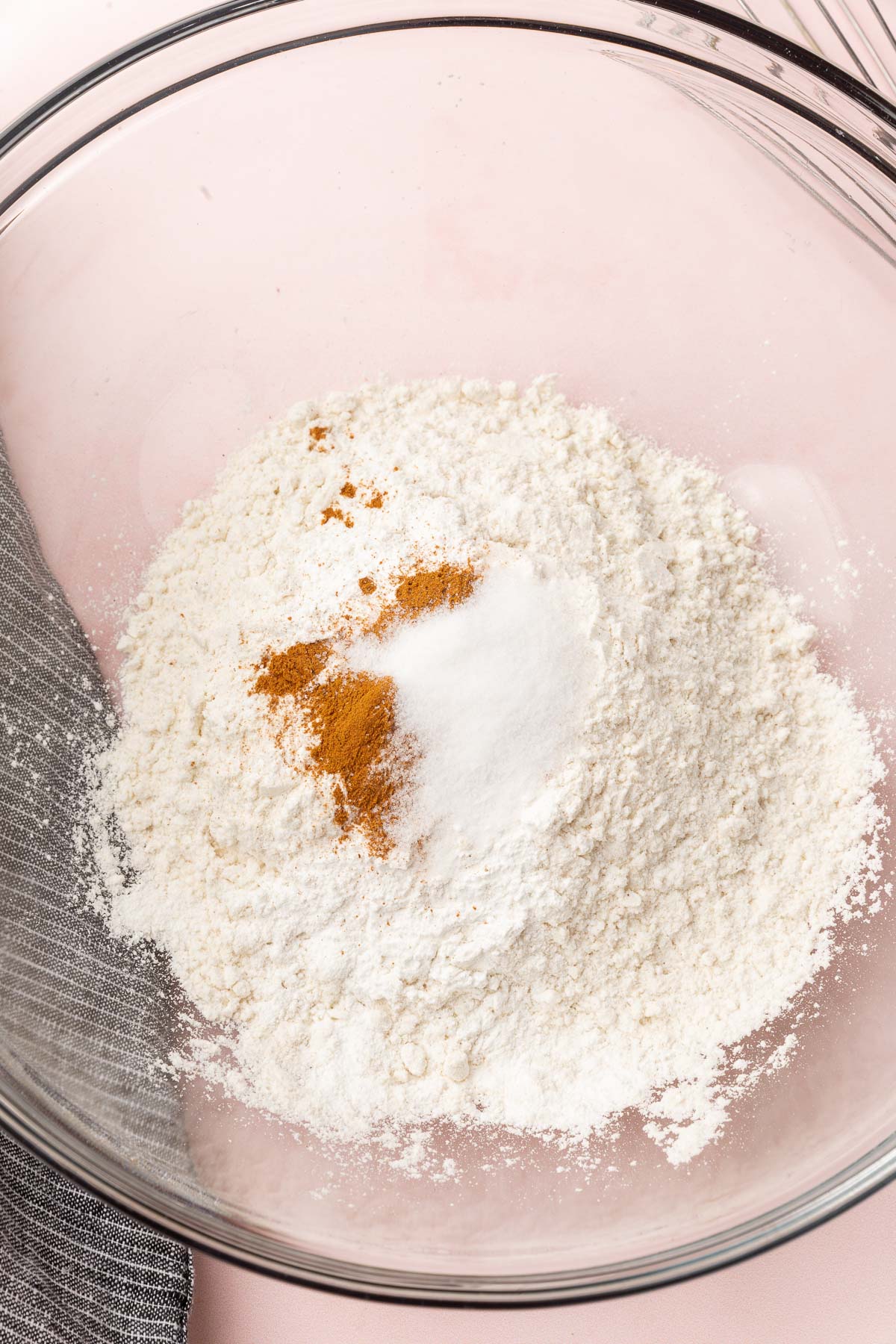 A glass mixing bowl with gluten-free flour, salt, baking soda, baking powder, and ground cinnamon in it.