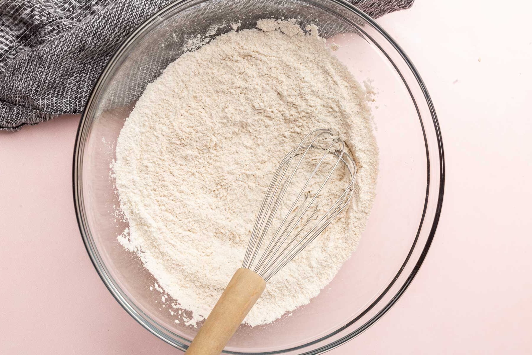A glass mixing bowl with gluten-free flour and a whisk in it.