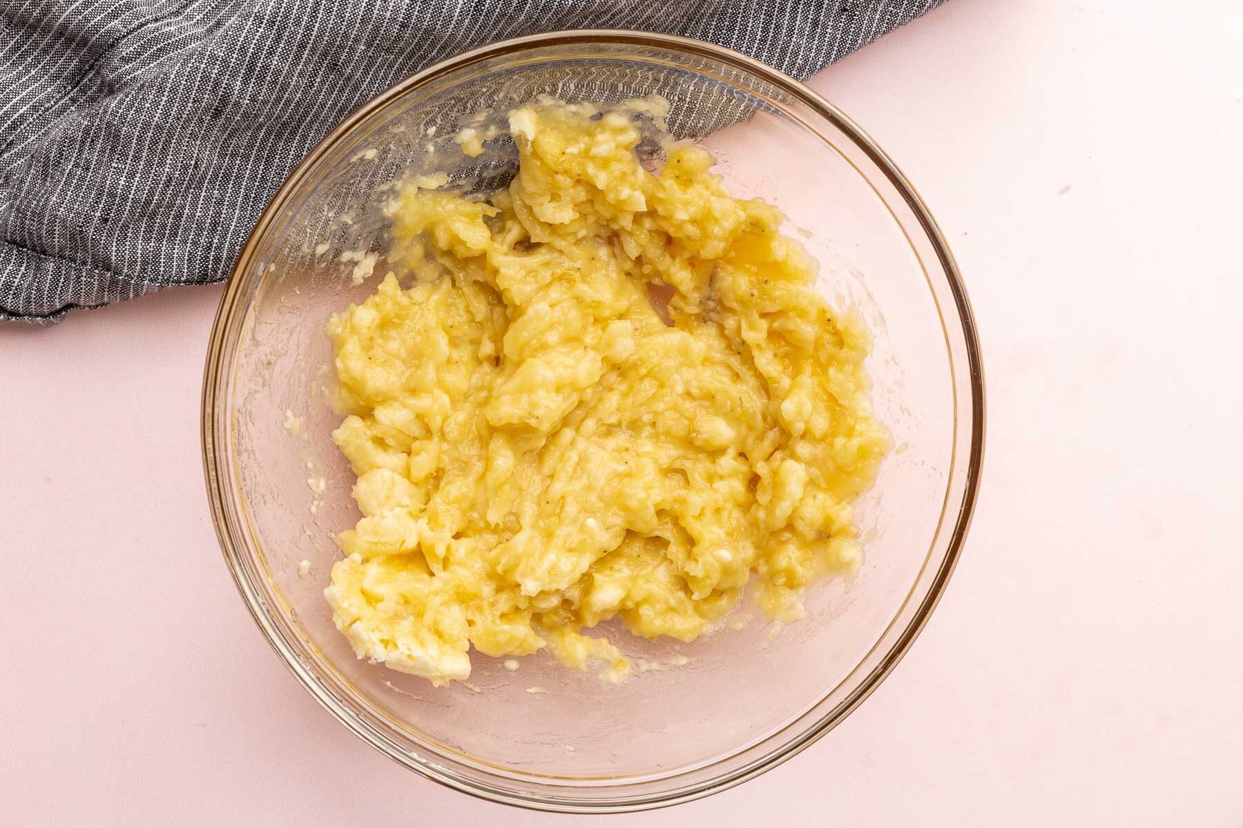 A glass mixing bowl with mashed banana in it.