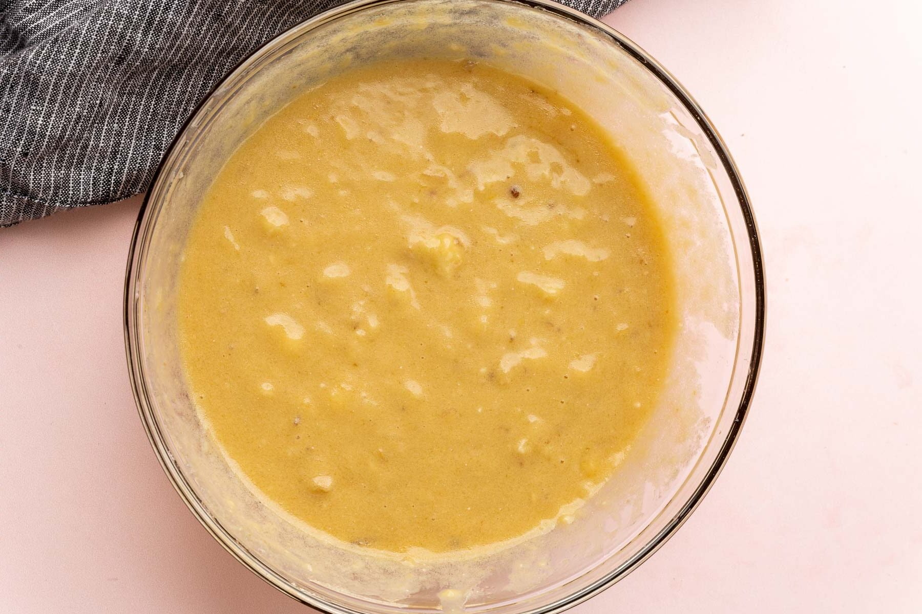 A glass mixing bowl with a mashed banana, brown sugar, oil, egg and vanilla extract mixture in it to make banana muffins.