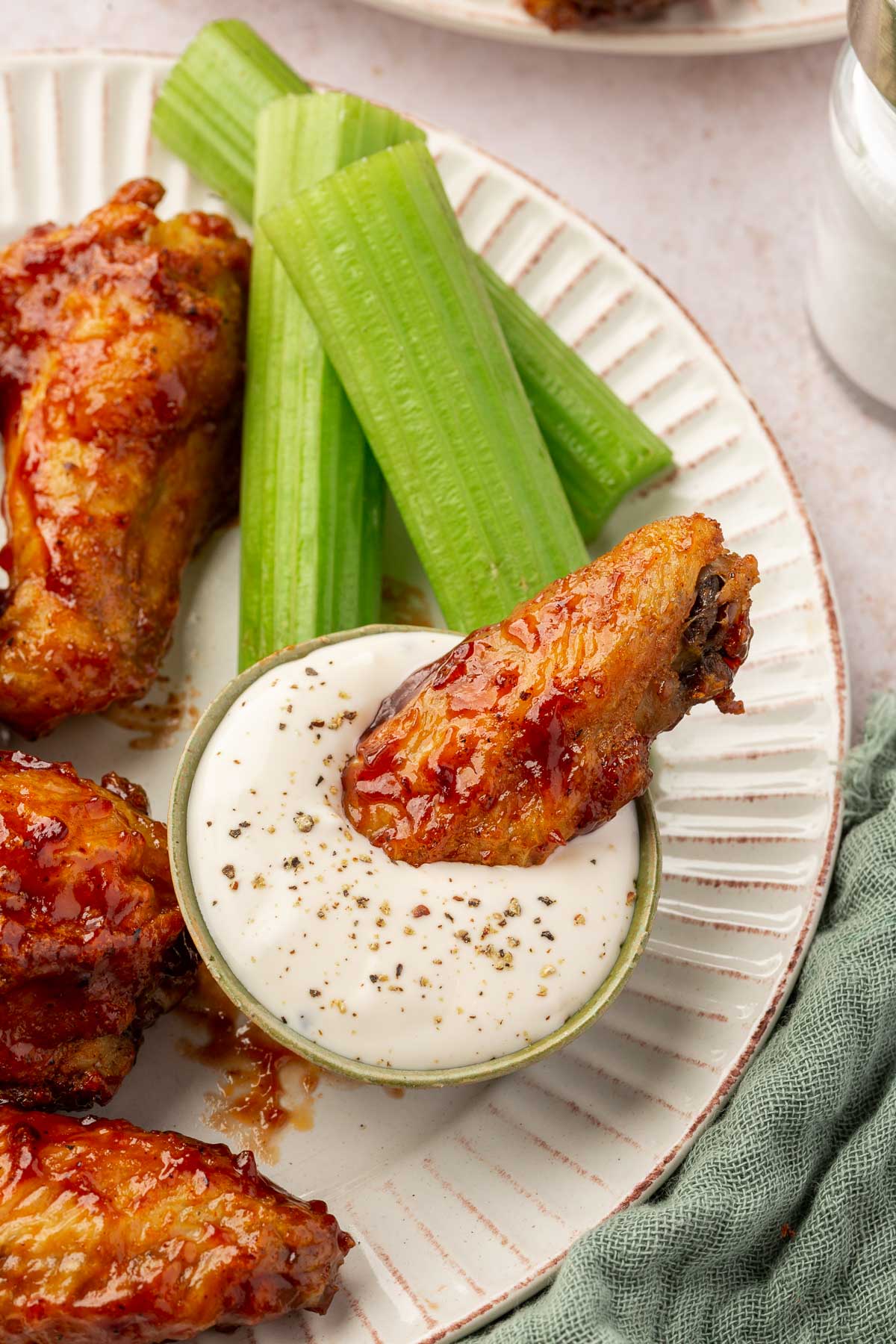 A BBQ chicken wing dipped into a small bowl of bleu cheese dressing with more gluten free chicken wings and a few pieces of celery on the side.