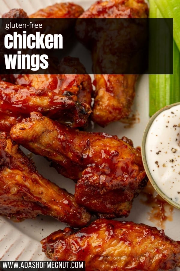 A close up of gluten free chicken wings tossed in BBQ sauce on a plate with pieces of celery and a small bowl of bleu cheese dressing on the side.