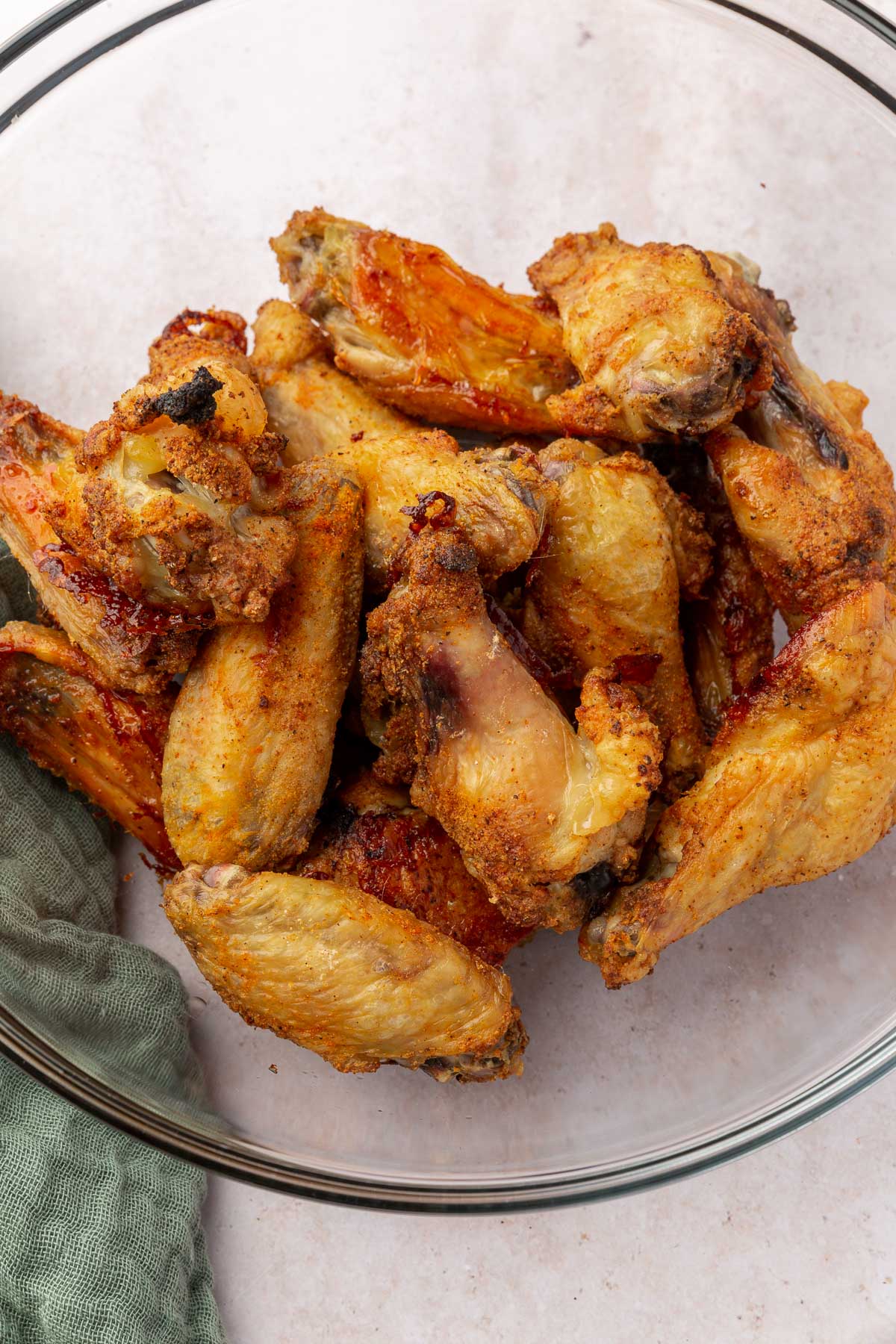 A glass mixing bowl with a pile of gluten-free chicken wings in it after baking in the oven.