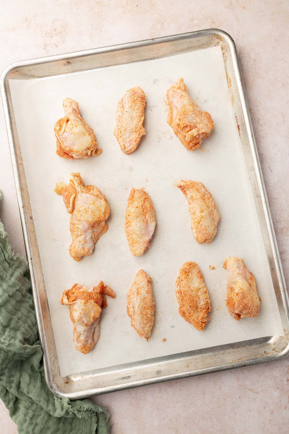 A baking sheet lined with parchment paper and topped with raw chicken wings before baking in the oven.
