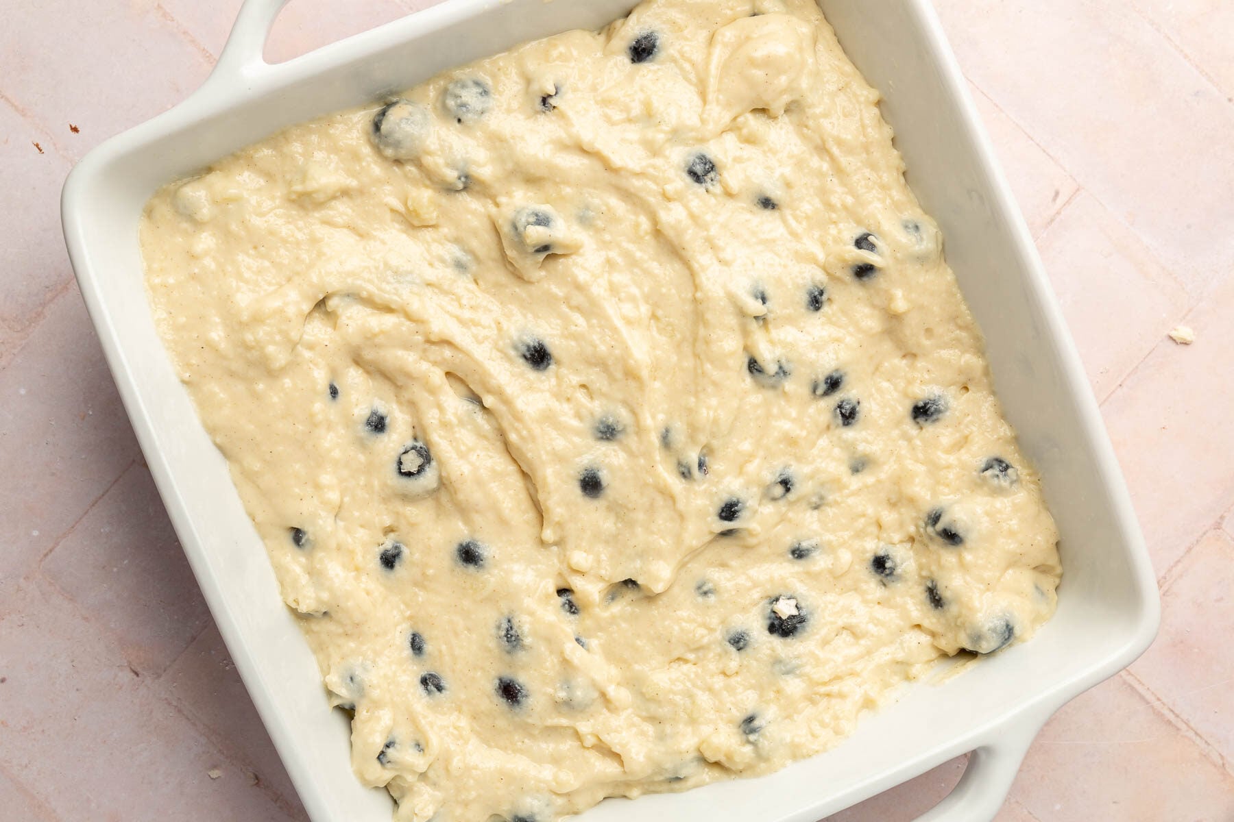 A ceramic 8x8-inch baking dish filled with blueberry coffee cake batter before baking in the oven.