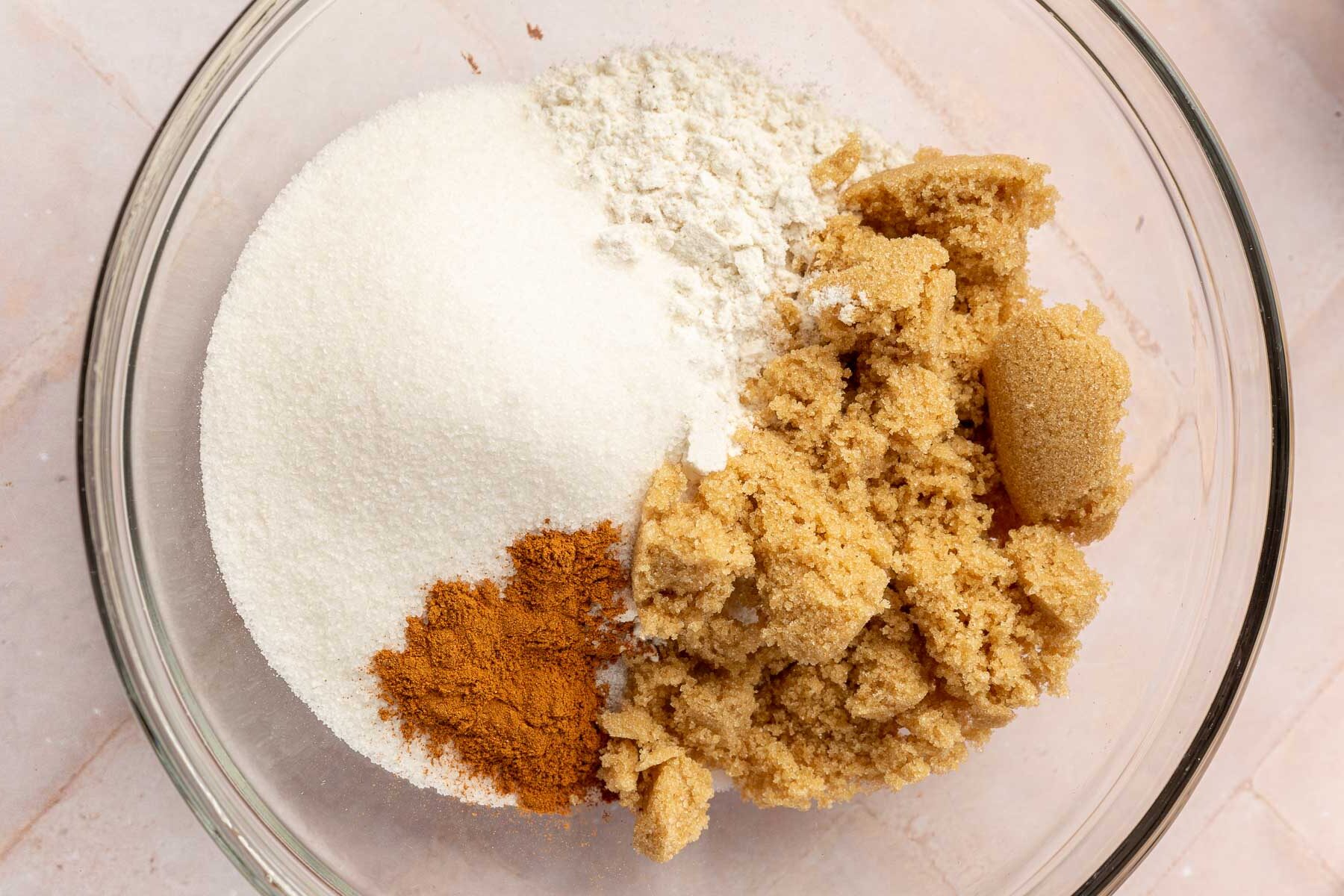 A glass mixing bowl with granulated sugar, flour, cinnamon and brown sugar in it to make a gluten free streusel topping.