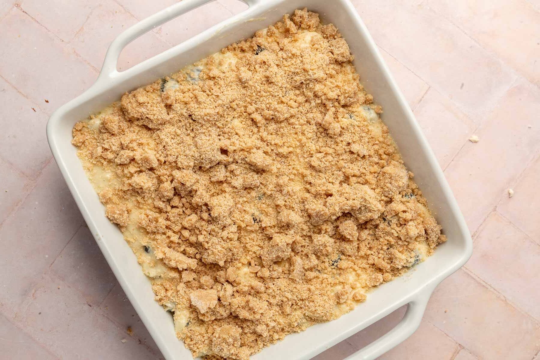 A ceramic 8x8-inch baking dish filled with blueberry coffee cake batter topped with gluten free streusel before baking in the oven.