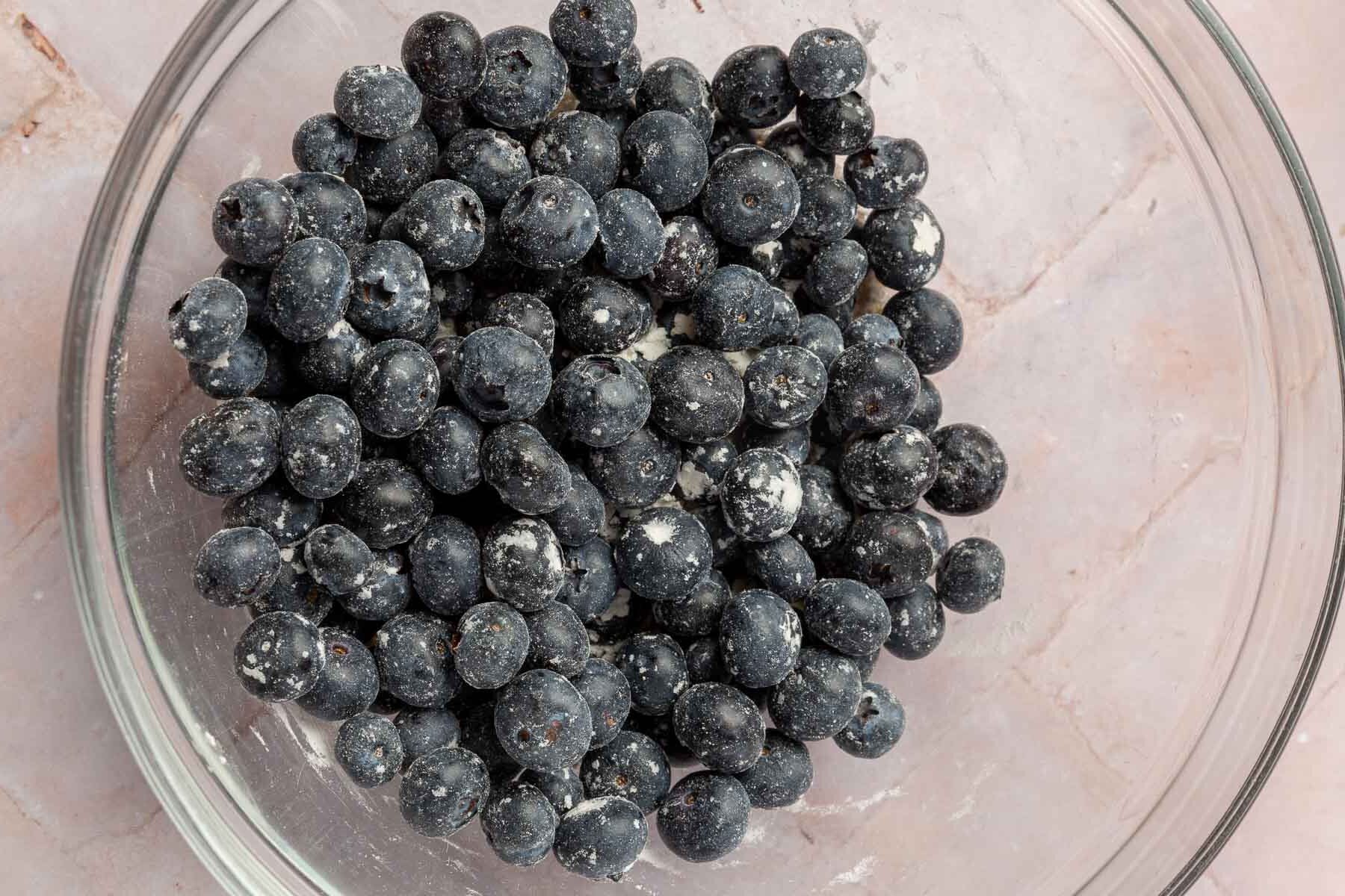 A glass mixing bowl of fresh blueberries tossed in gluten free flour.