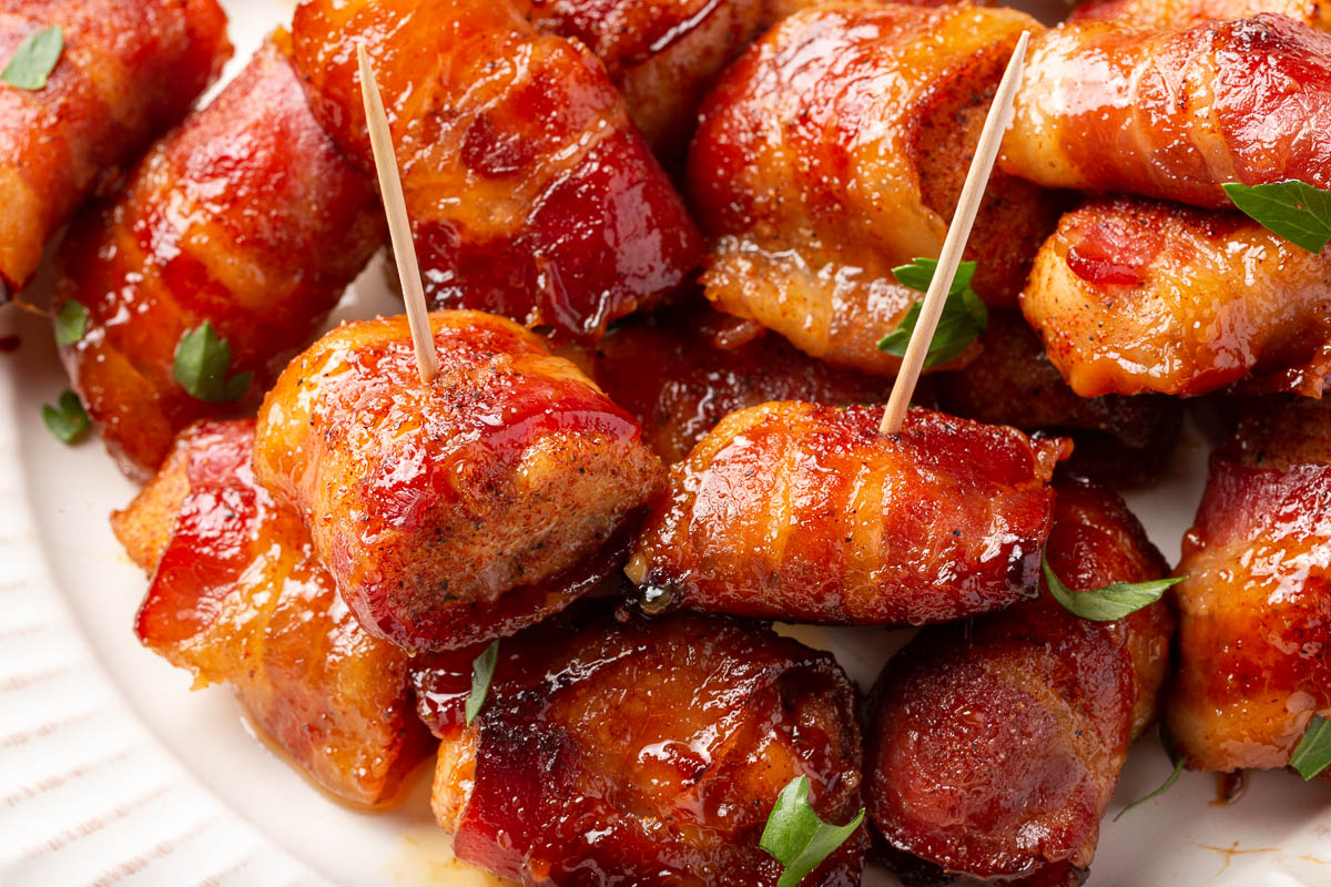 A pile of bacon wrapped chicken bites on a plate with a few toothpicks in a few of the chicken bites.