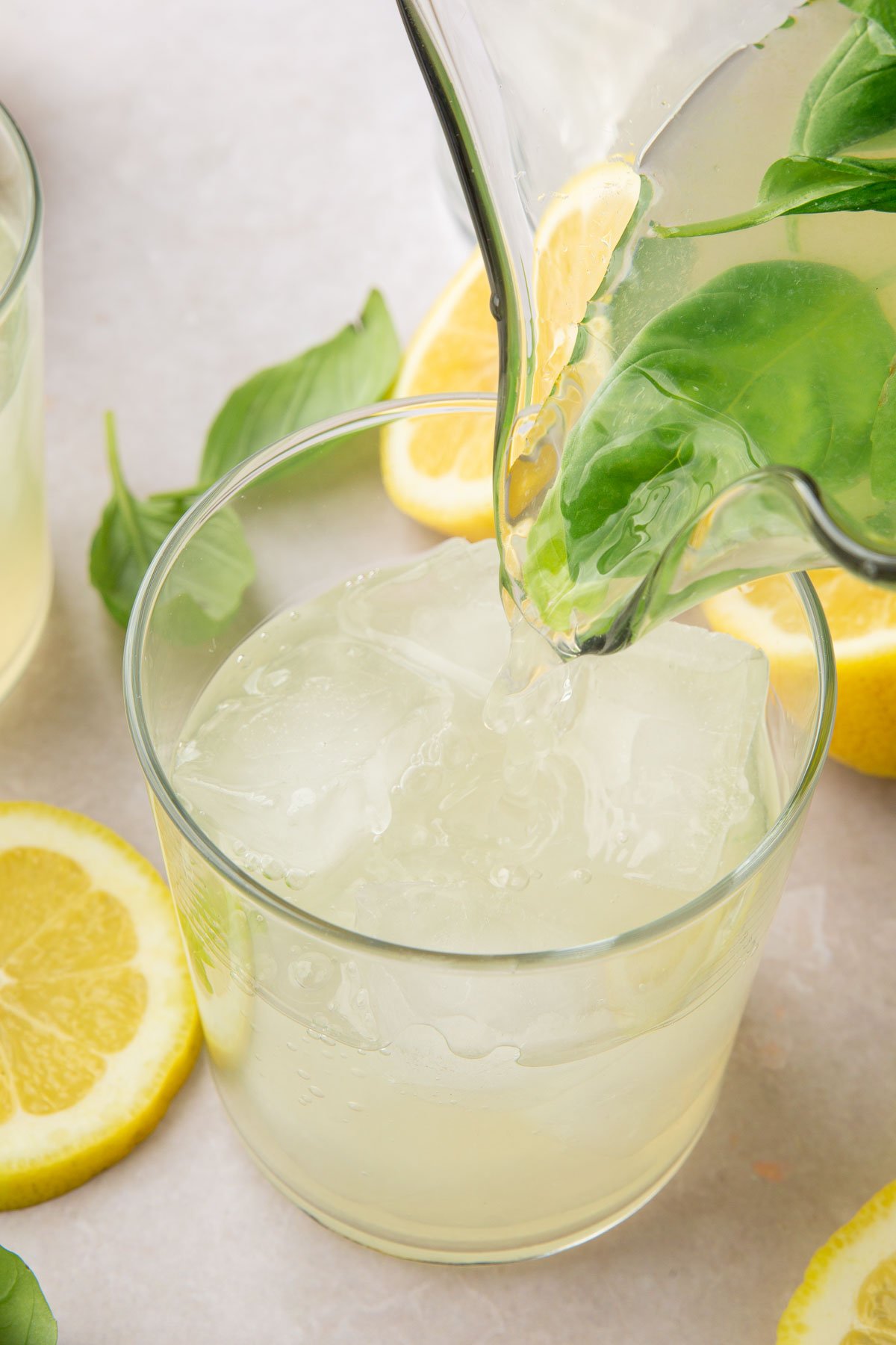 A pitcher pouring basil lemonade into a glass filled with ice.