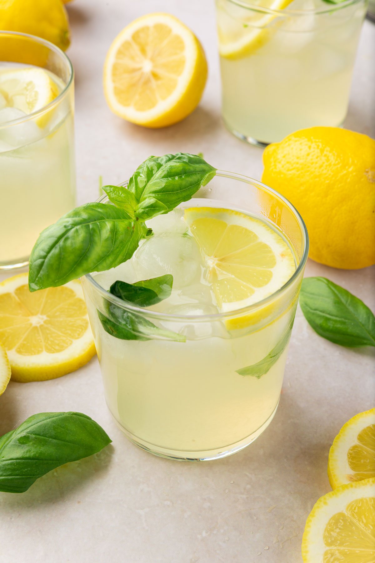 A glass of basil lemonade with fresh lemon slices and fresh basil with additional glasses of lemonade surrounding it.