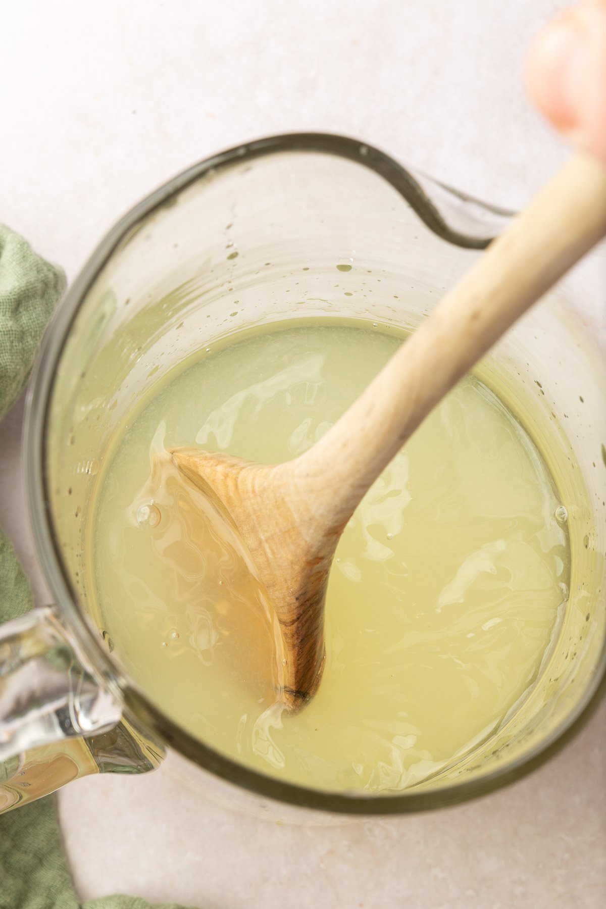 A wooden spoon stirring lemonade in a glass pitcher.