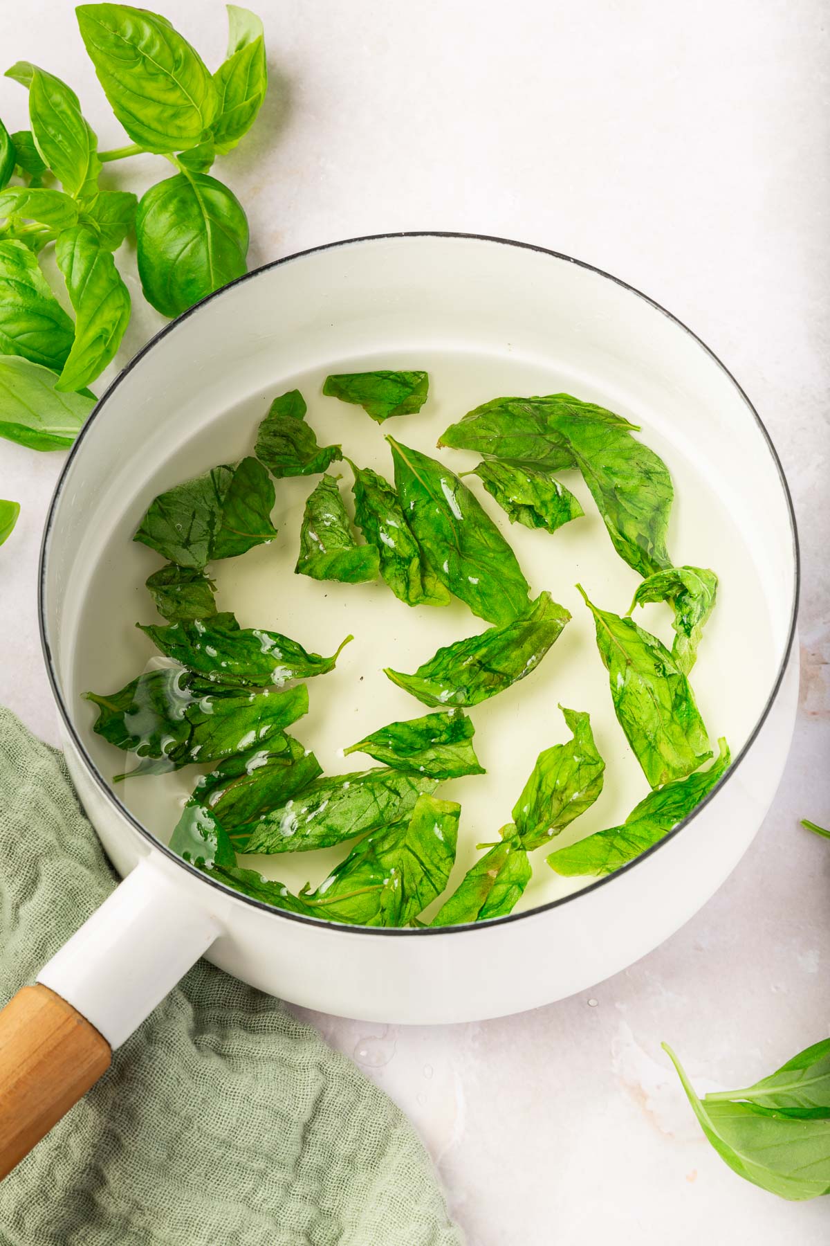 A saucepan with basil simple syrup in it with fresh basil leaves.