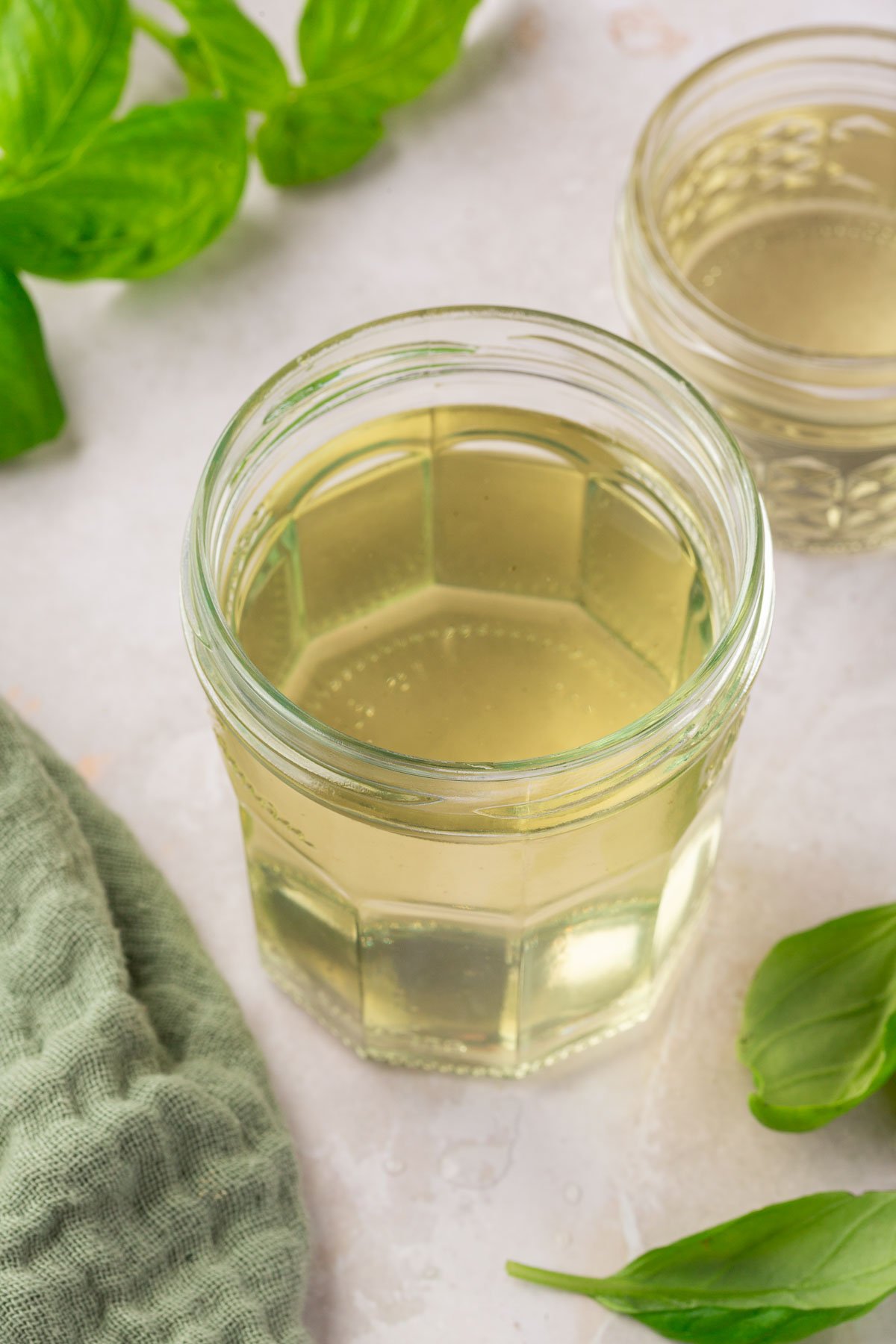 A glass jar of basil simple syrup with fresh basil leaves surrounding it.