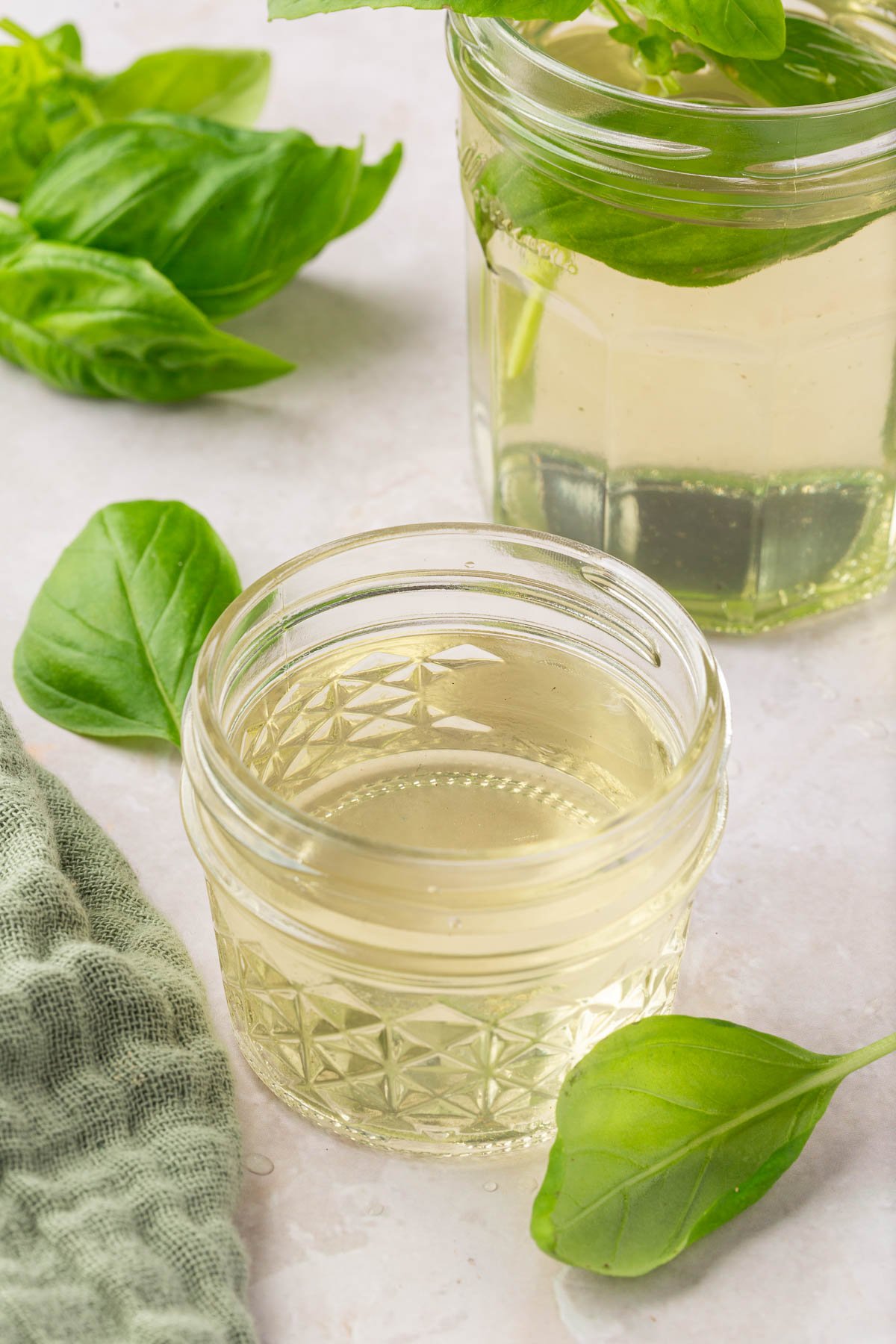 Two jars of basil simple syrup with fresh basil leaves surrounding them.