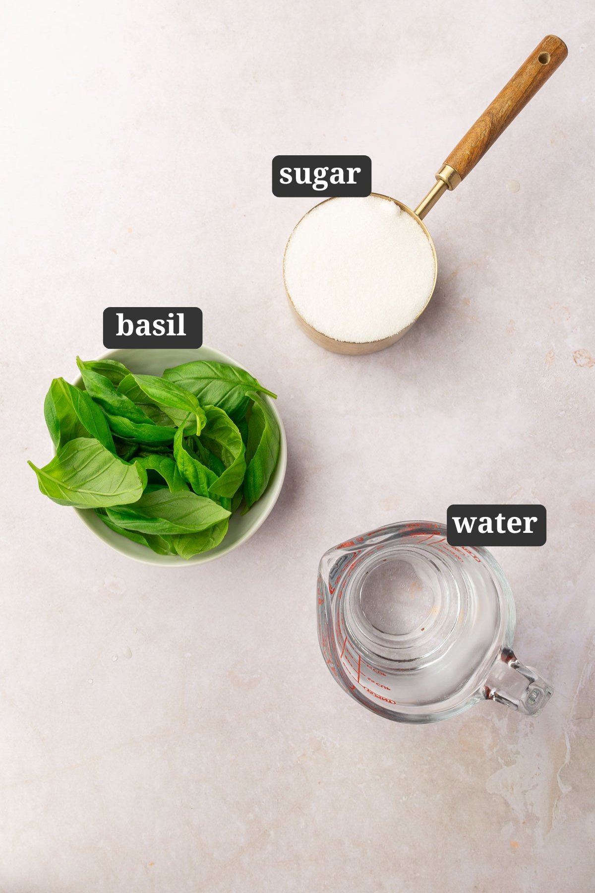 An overhead view of ingredients in small bowls to make basil simple syrup including basil, sugar and water with text overlays over each ingredient.
