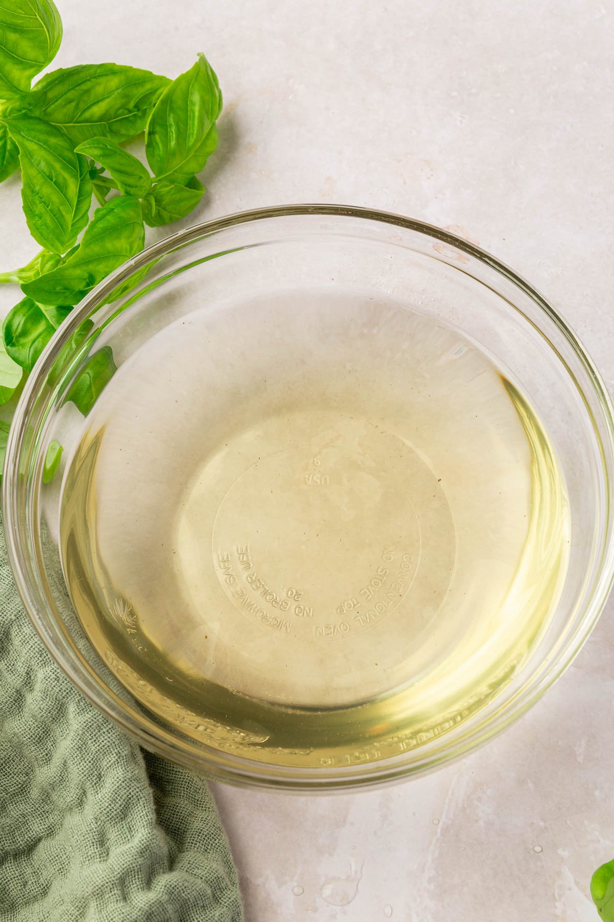 A glass bowl of basil simple syrup on a table with a green linen napkin and fresh basil leaves.