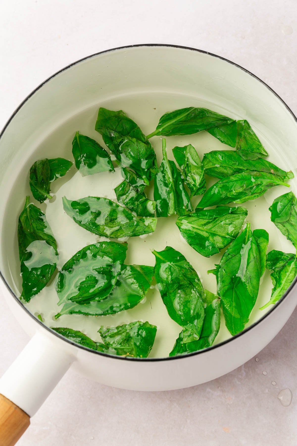 A white saucepan with basil simple syrup in it.