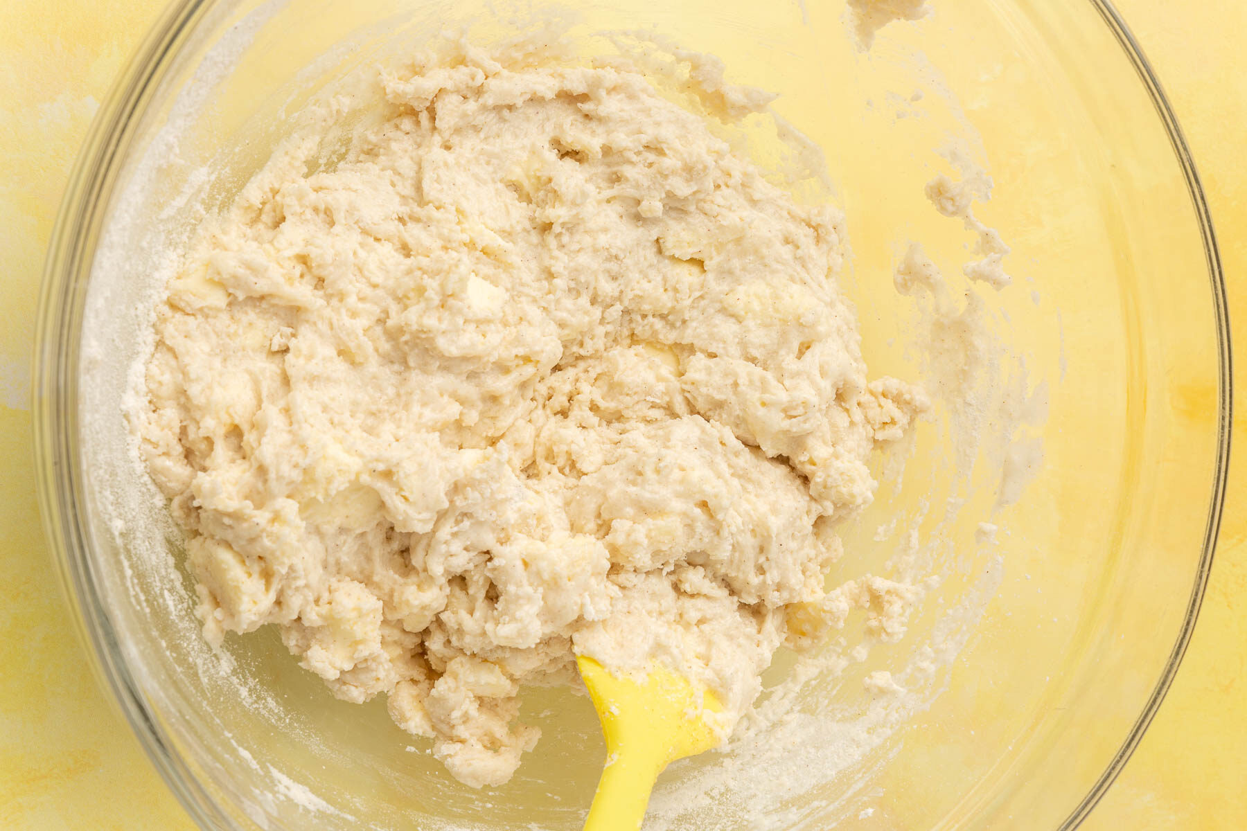 A gluten free biscuit dough in a glass mixing bowl on a yellow table.