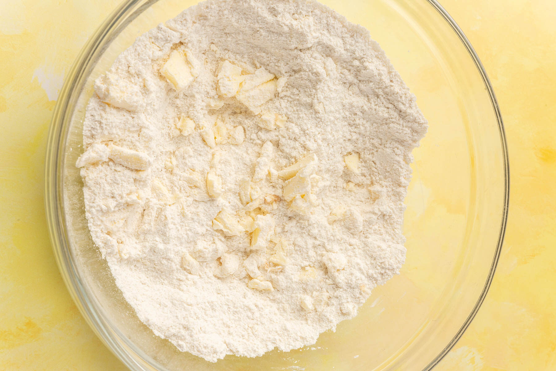 A glass mixing bowl with gluten-free flour blend with chunks of butter cut into it.