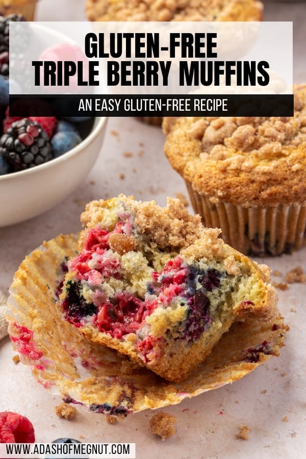 Half of a gf mixed berry muffin that has been bitten into and is laying on the muffin liner with additional muffins and streusel crumbs in the background.