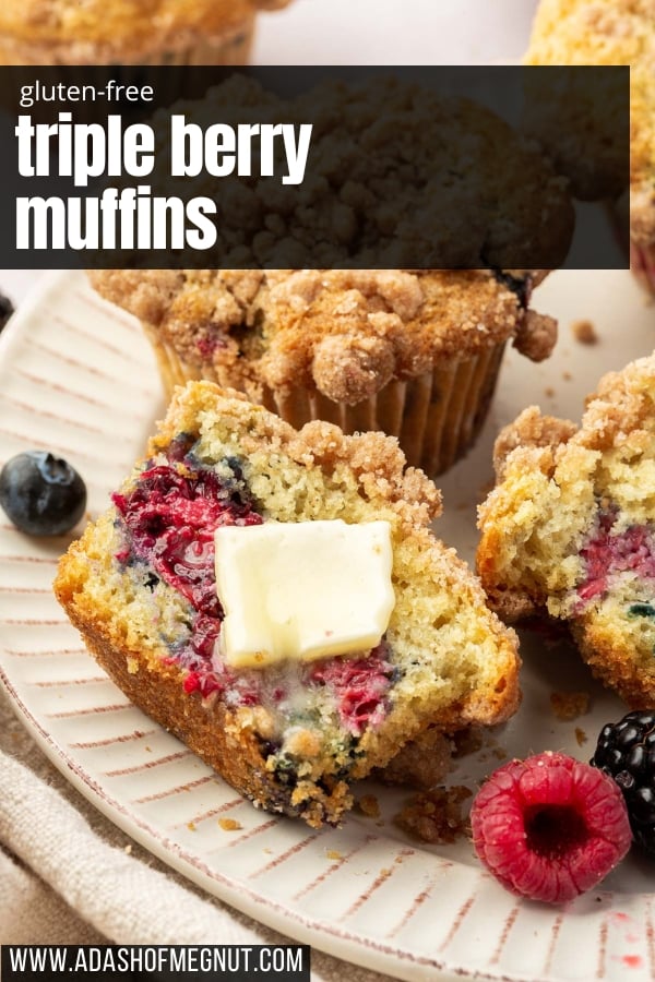 Half of a gluten free triple berry muffin on a plate with a pat of melted butter on it with additional muffins and fresh berries on the plate.