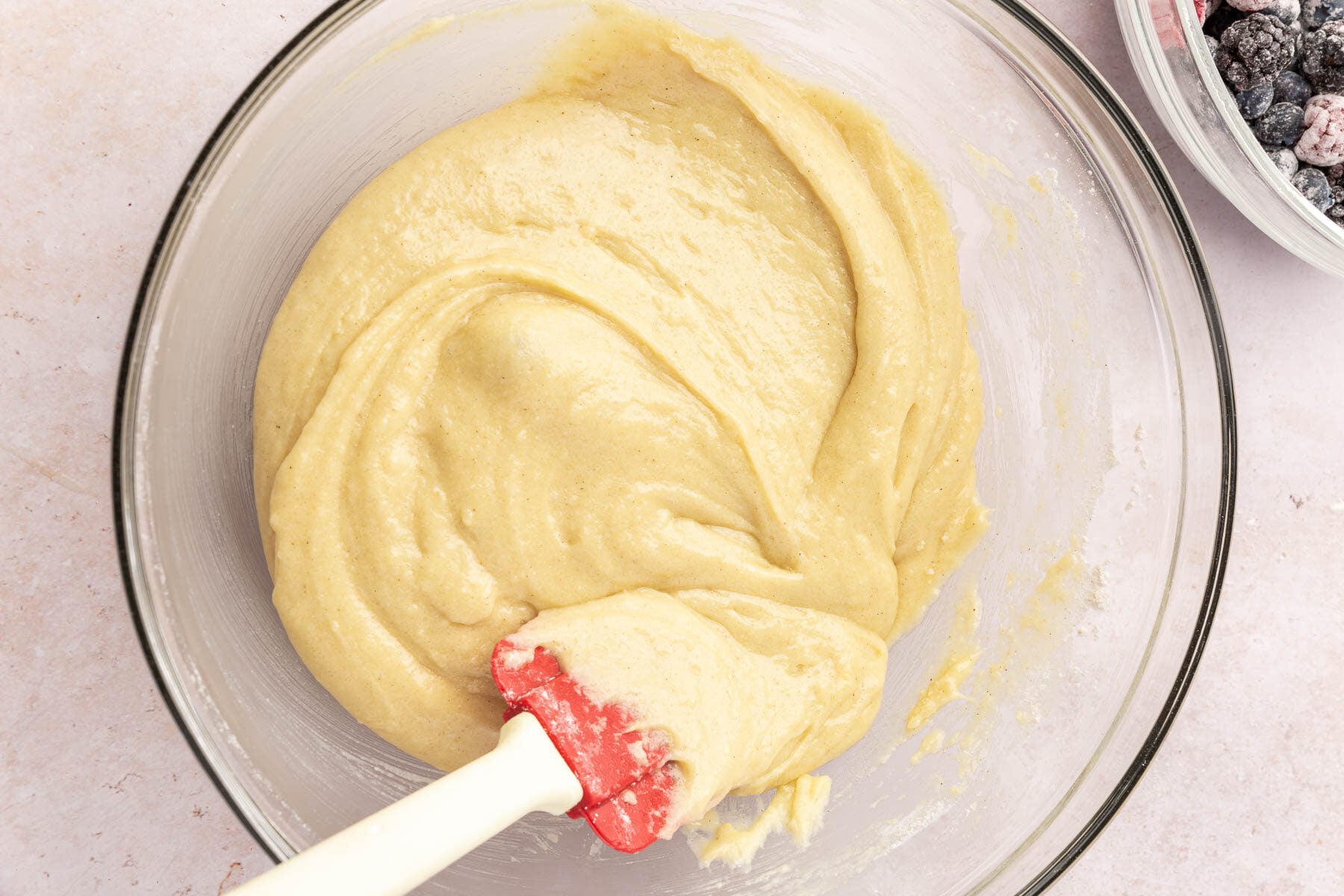 A glass mixing bowl with gluten-free muffin batter in it being stirred by a rubber spatula.